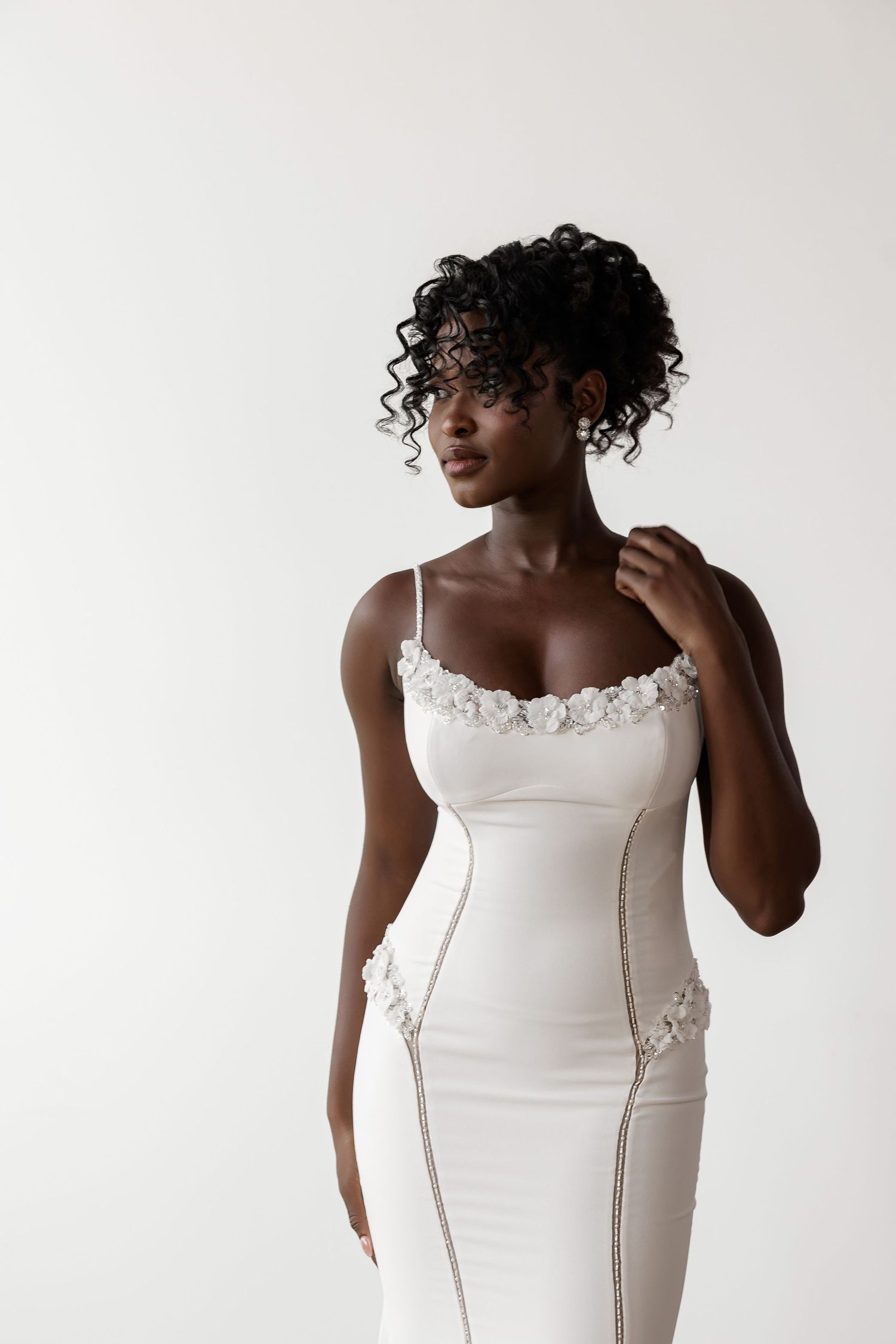 Sleek white wedding dress with lace applique details shown in modern studio setting.