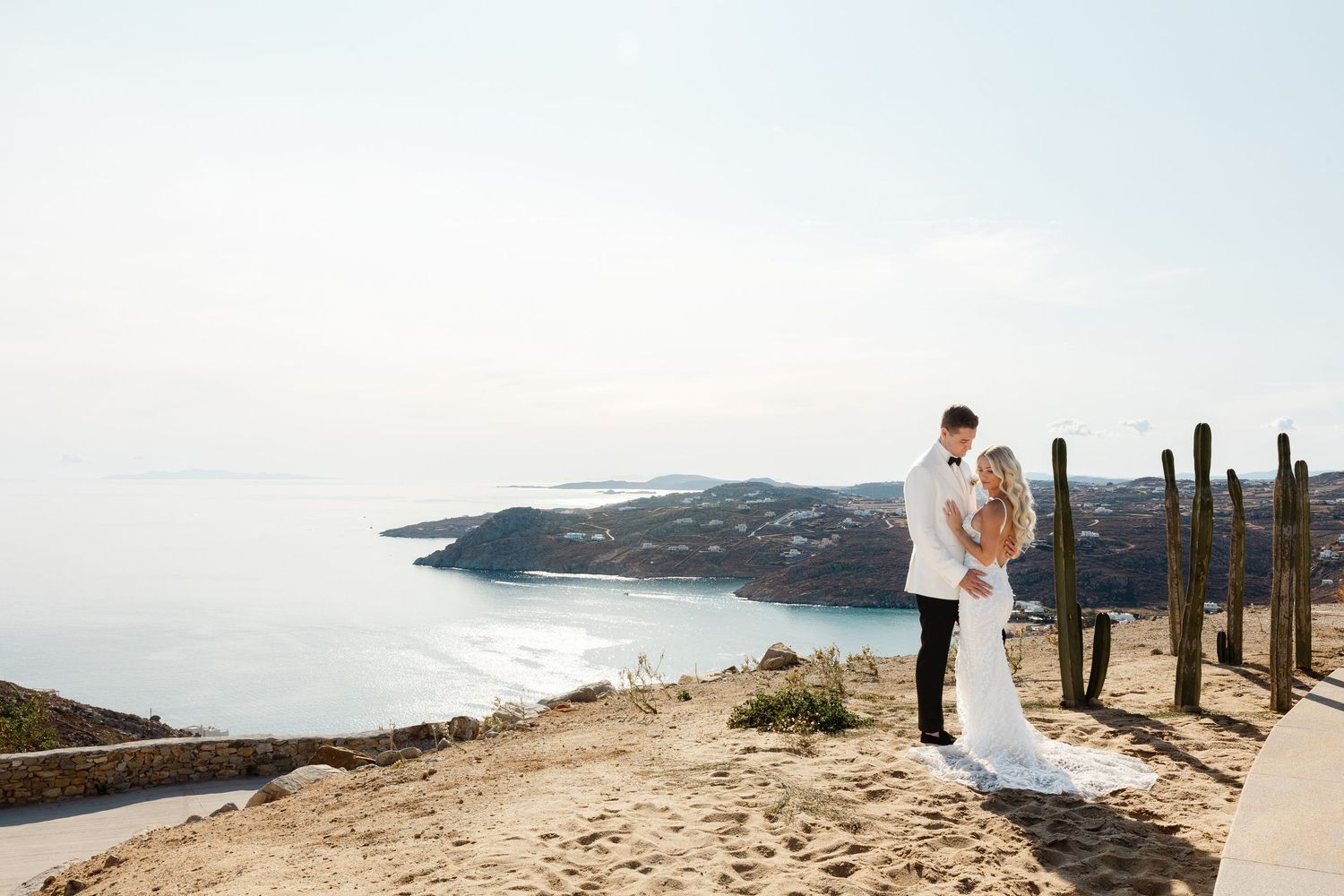 A wedding couple poses against a scenic coastal desert landscape with tall cacti.