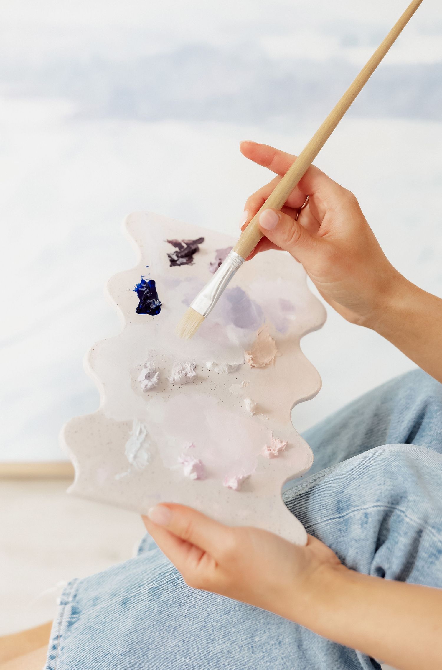 Close-up of hands holding paint palette and brush with purple tones.
