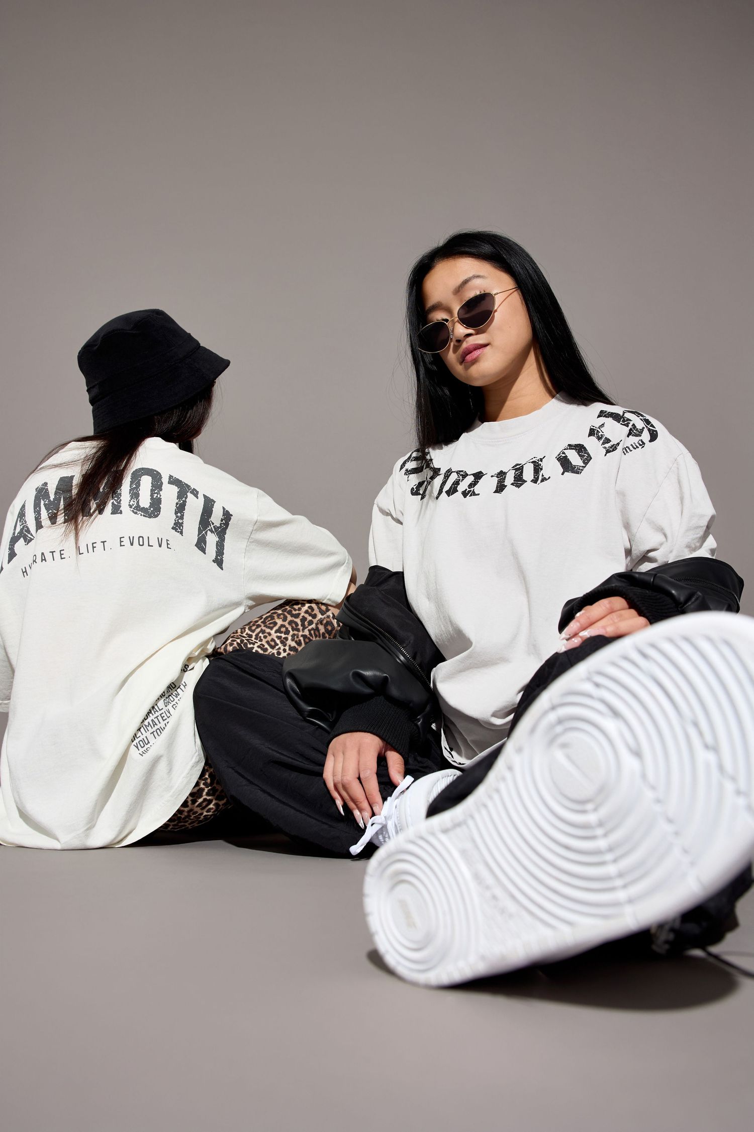 Models in white t-shirts and black clothing pose on floor with white circular prop.