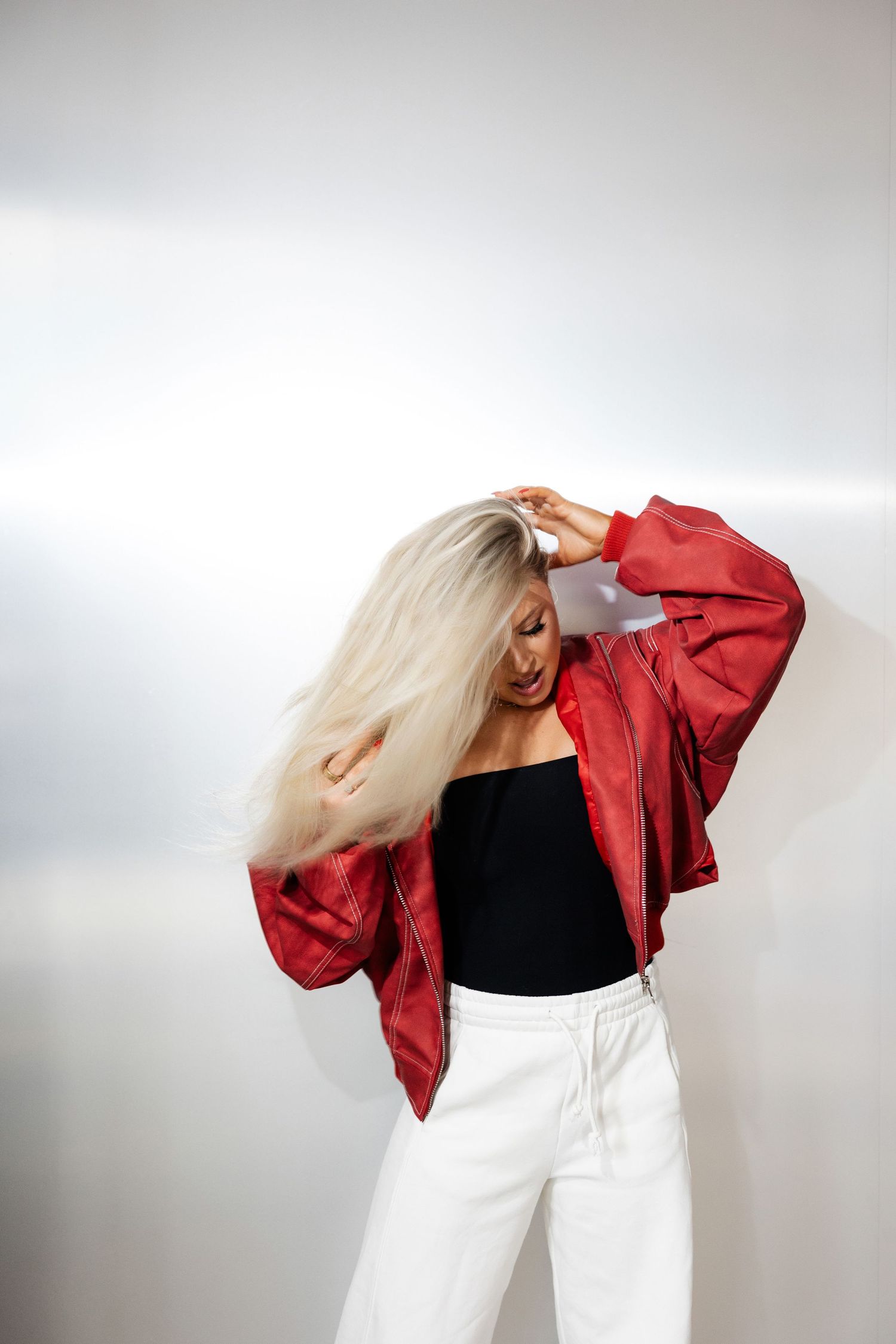 Model in red jacket and white pants creates movement-based poses in studio setting.