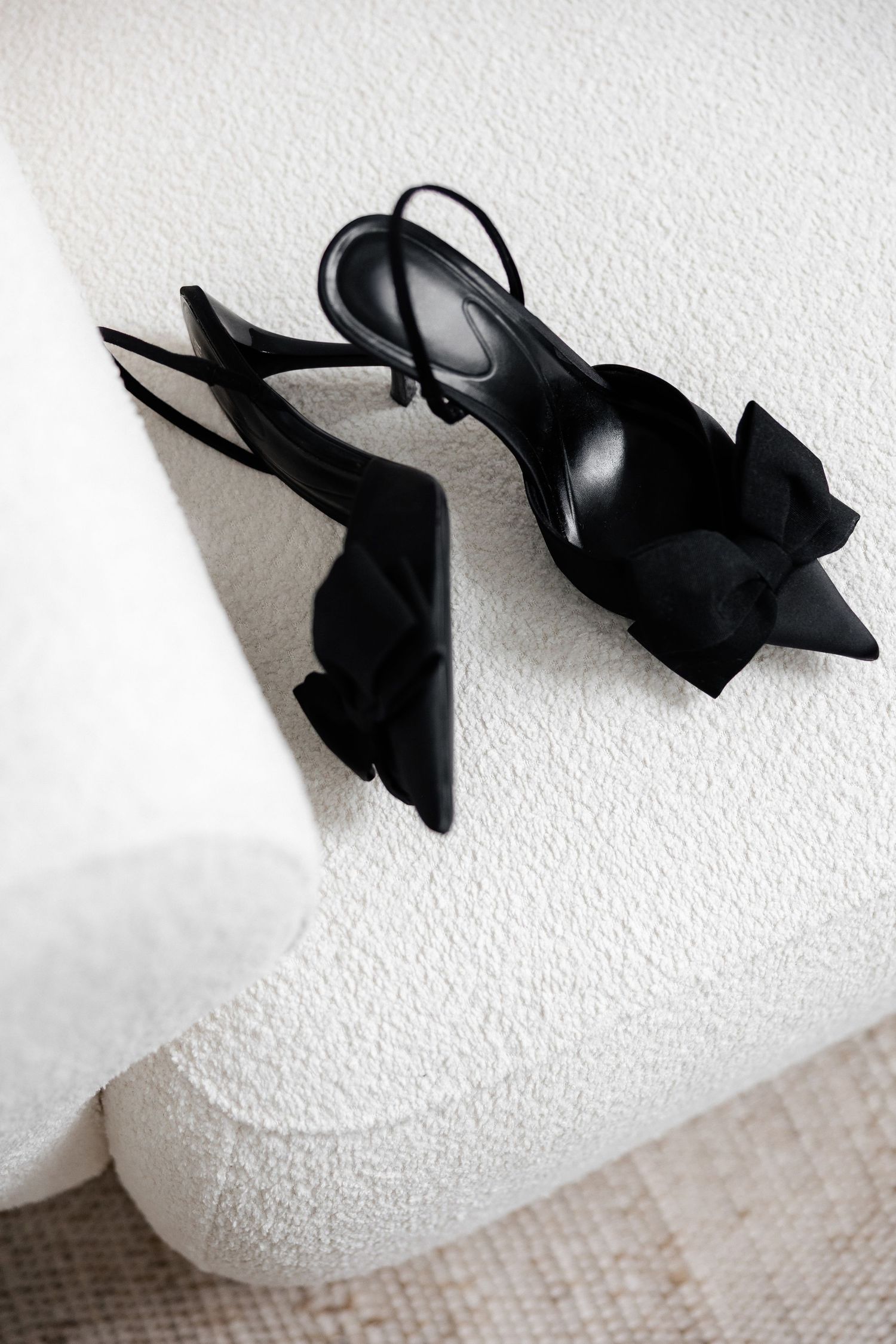 Elegant black stiletto heels arranged in a minimalist sequence on white textured surface.