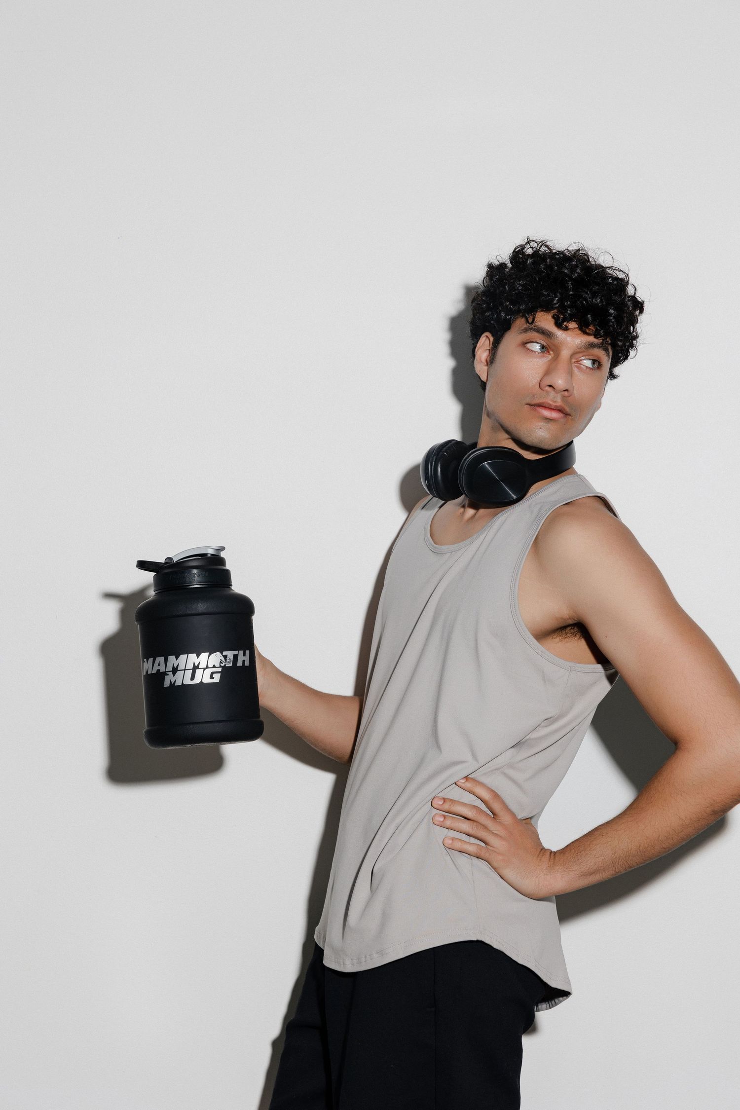 Person in gray tank top poses with black fitness container against white background.