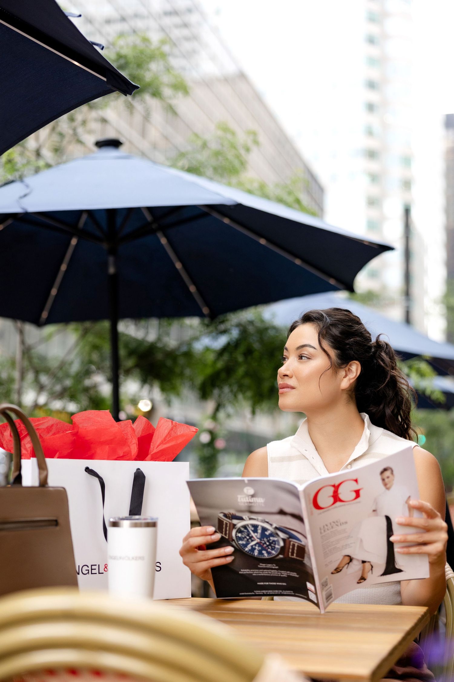 Person relaxing under black patio umbrellas at an outdoor cafe table.