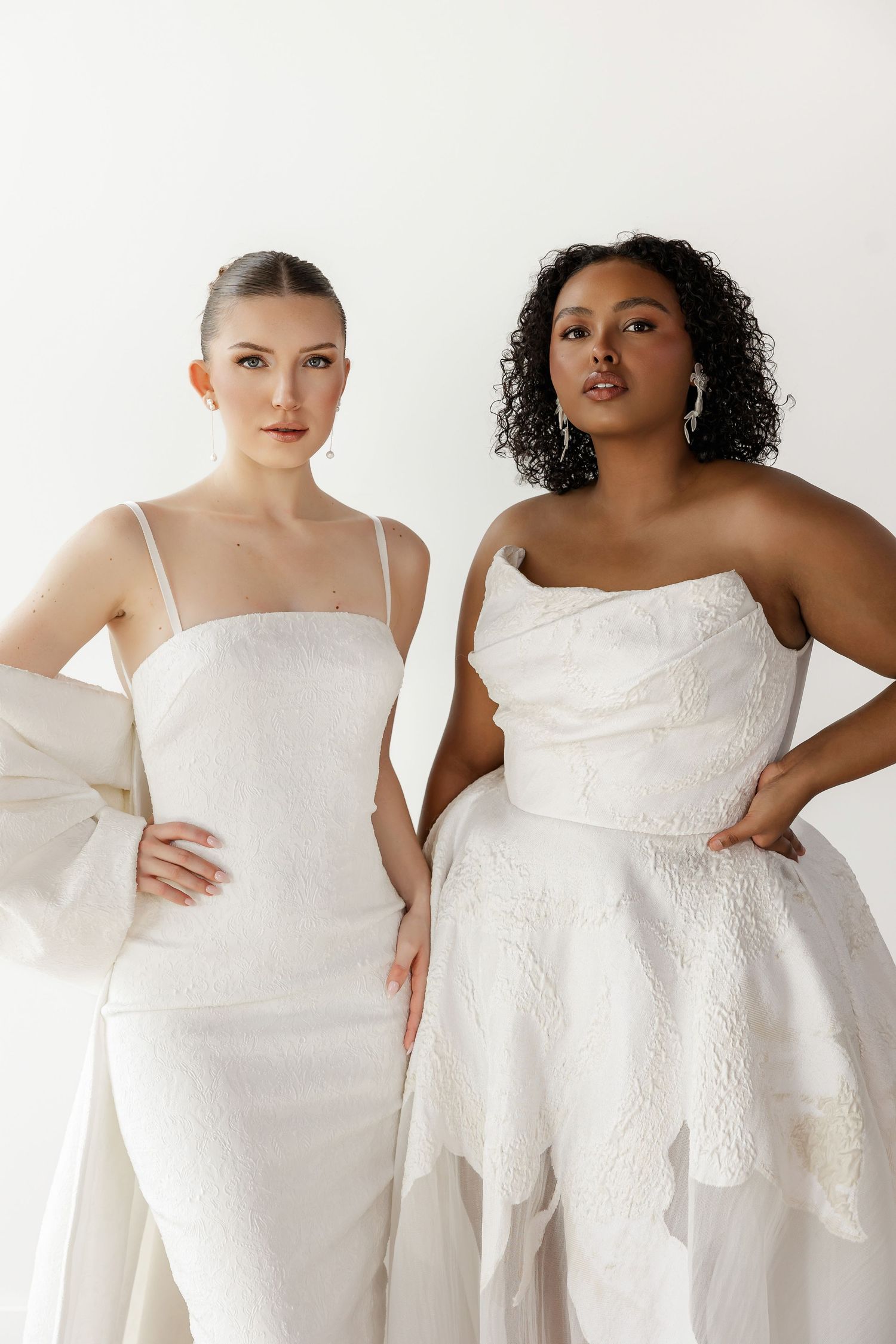 Models display modern white wedding gowns with structured bodices in studio setting.