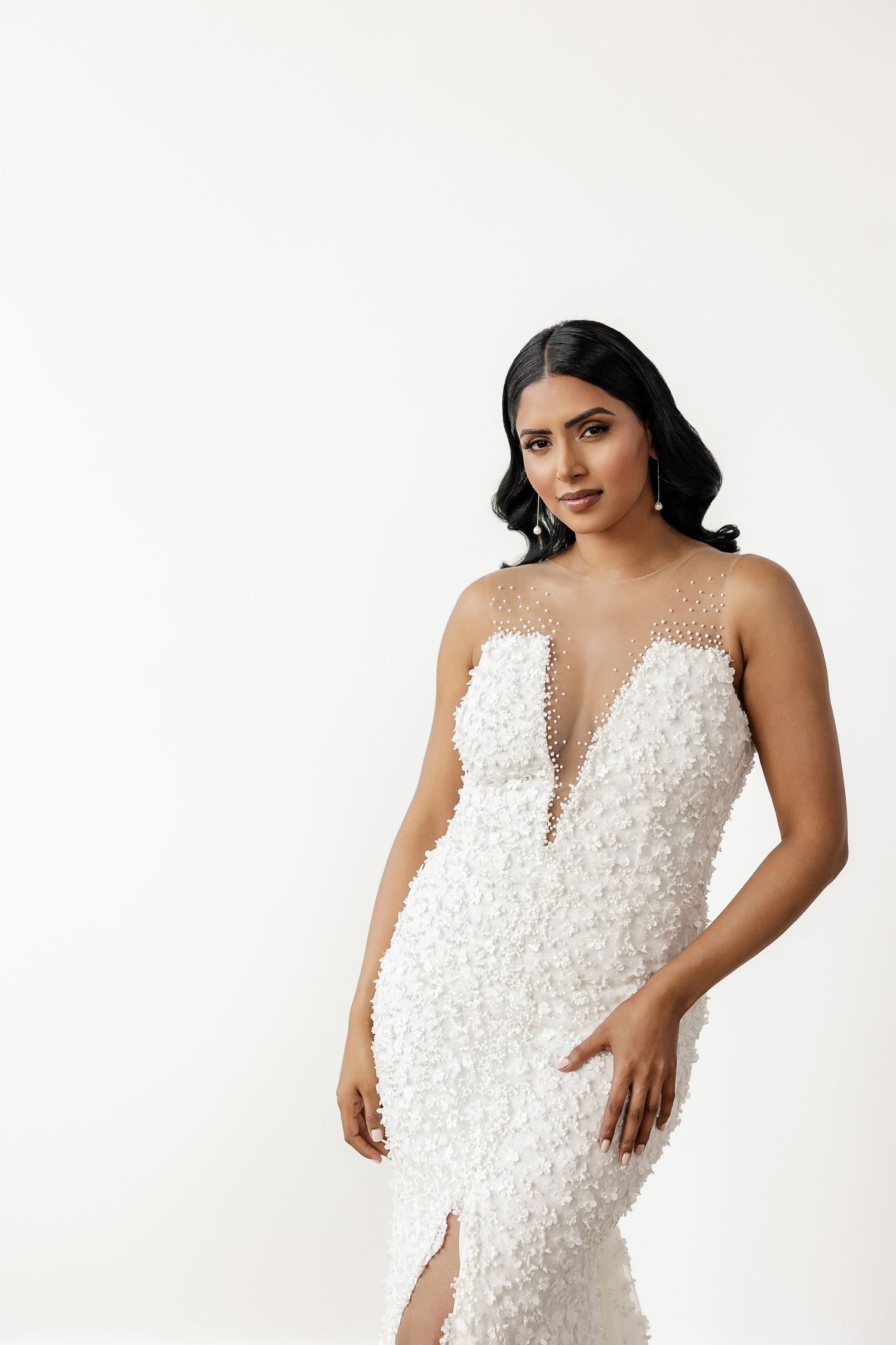 Bridal fashion shoot featuring pearl-embellished white wedding gown against white background.