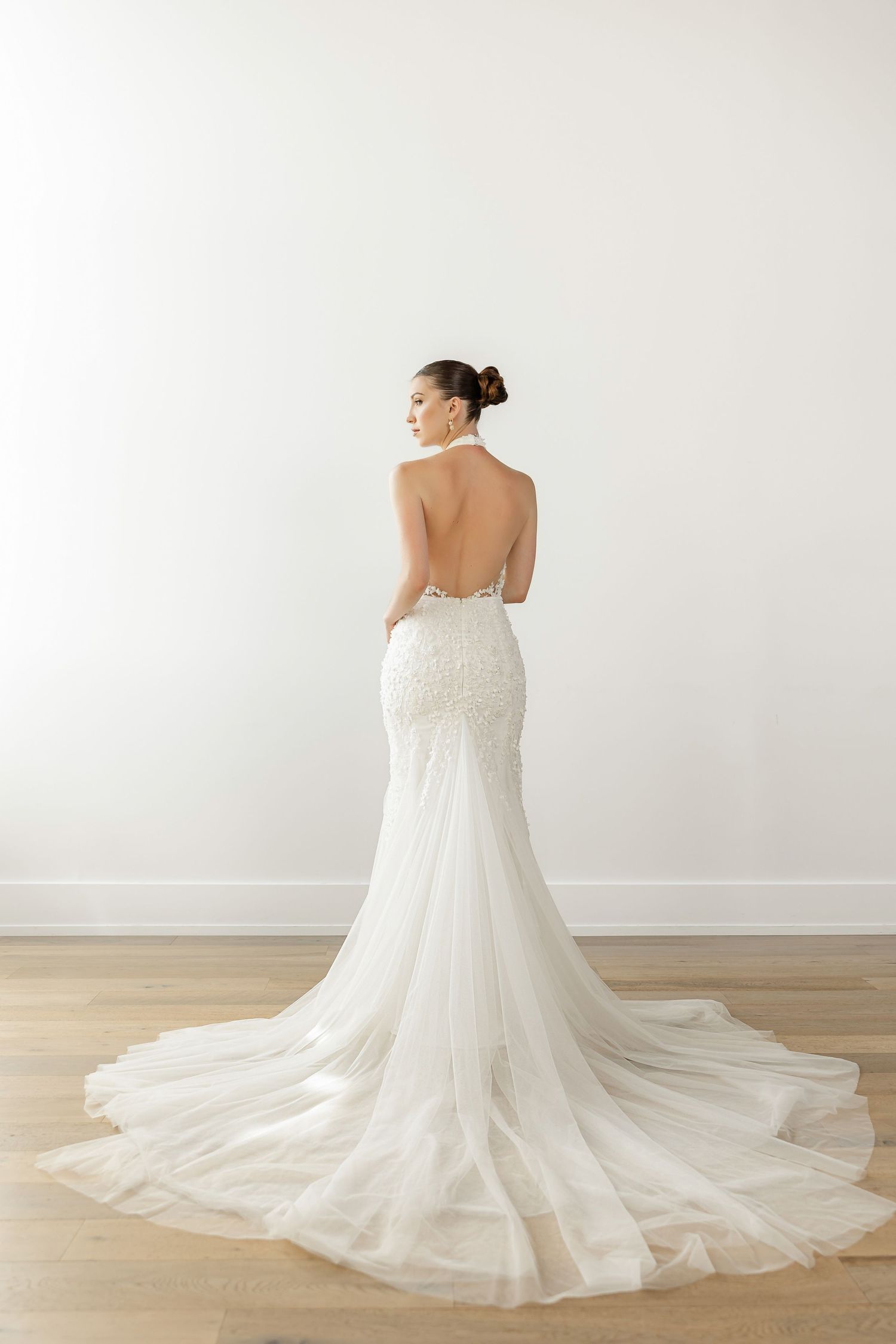 Elegant white wedding dress with flowing train shown from behind against white backdrop.