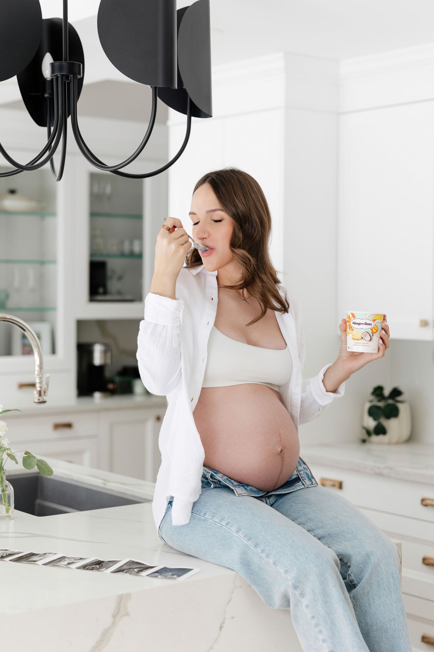 Woman enjoying snack while sitting on kitchen counter during maternity shoot.