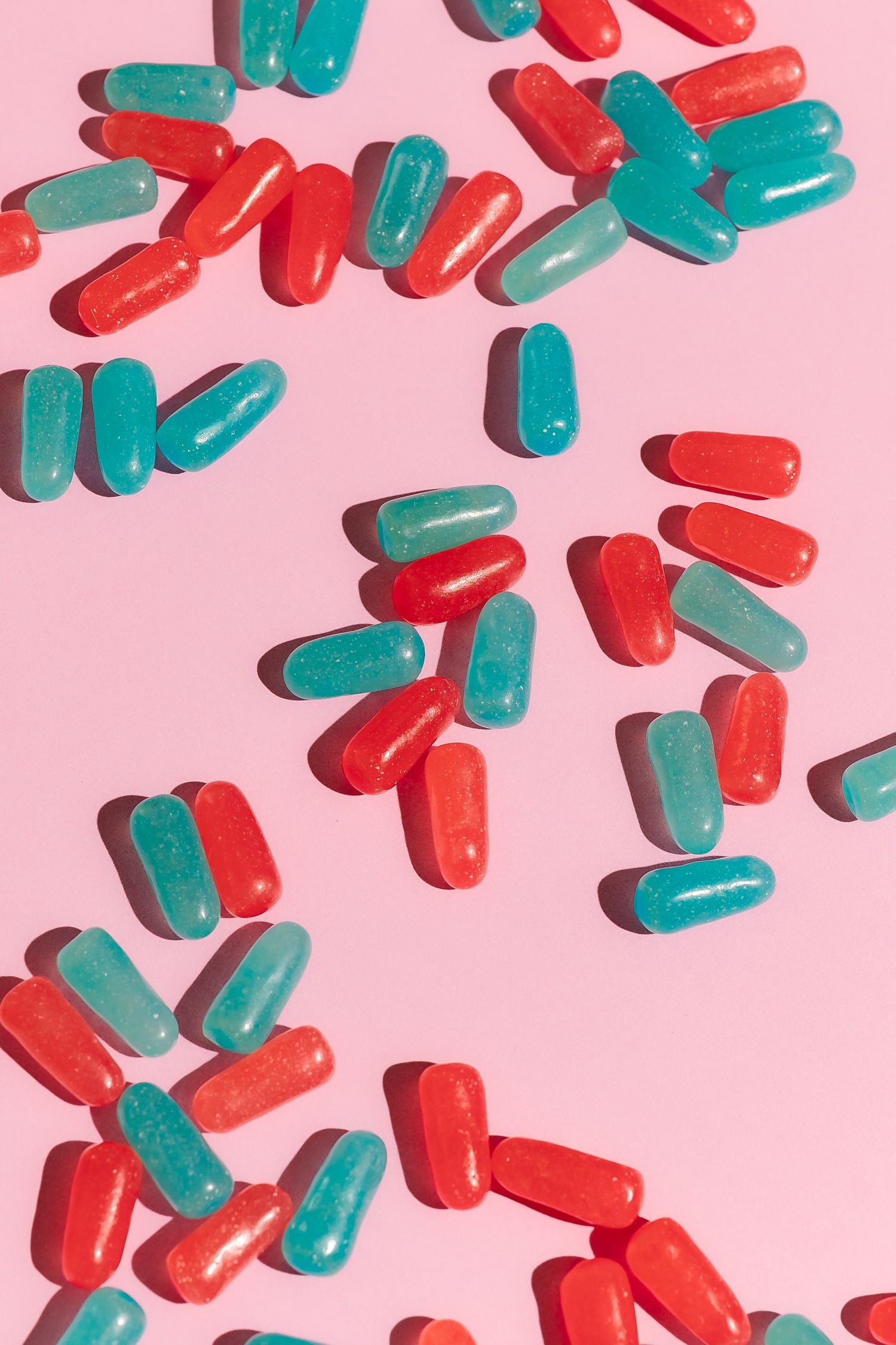 Red and teal jelly candies arranged on pink background.