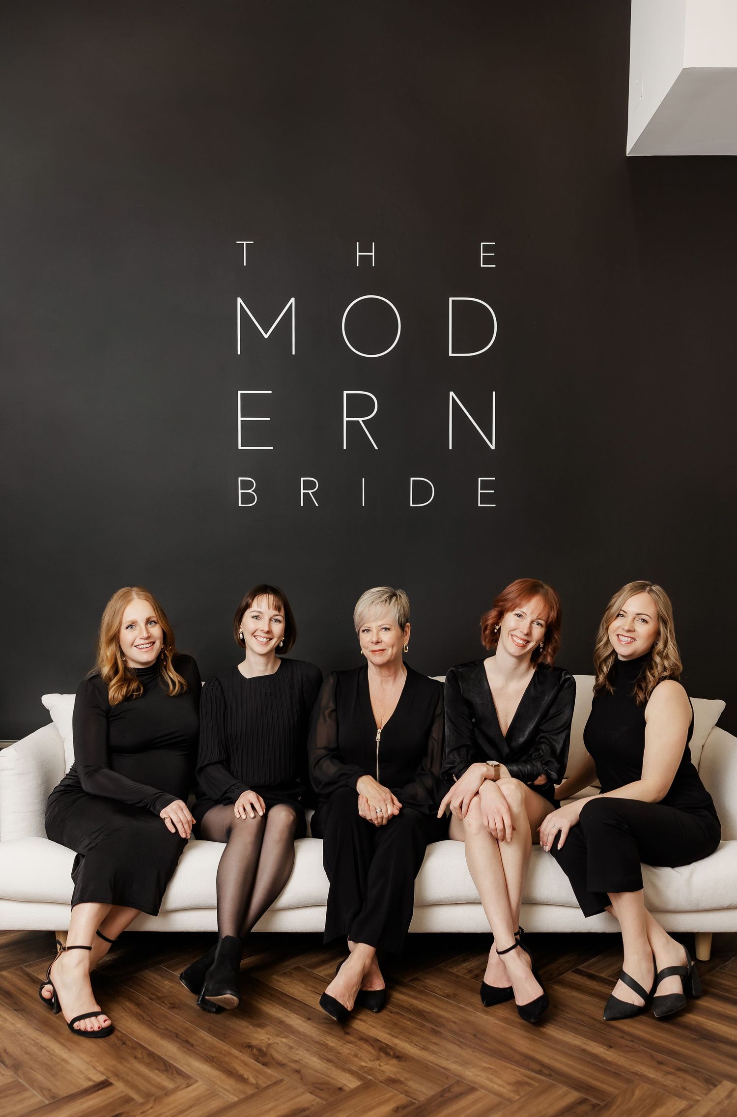 Modern bridal boutique staff sitting on white couch with text 'THE MODERN BRIDE' on wall.