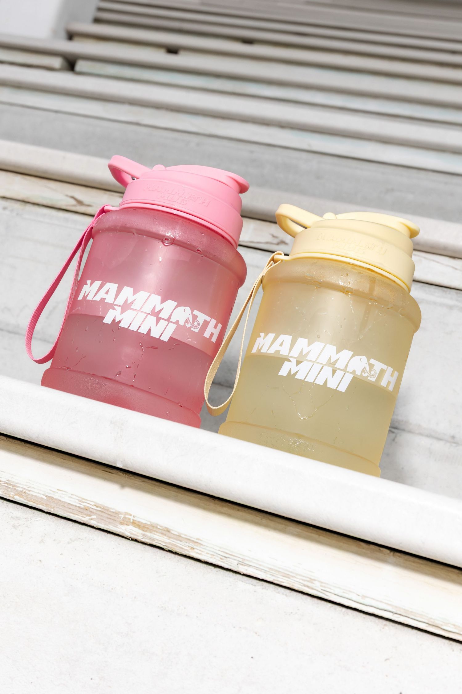 Pink and beige water bottles with white text branding lined up on white surface.