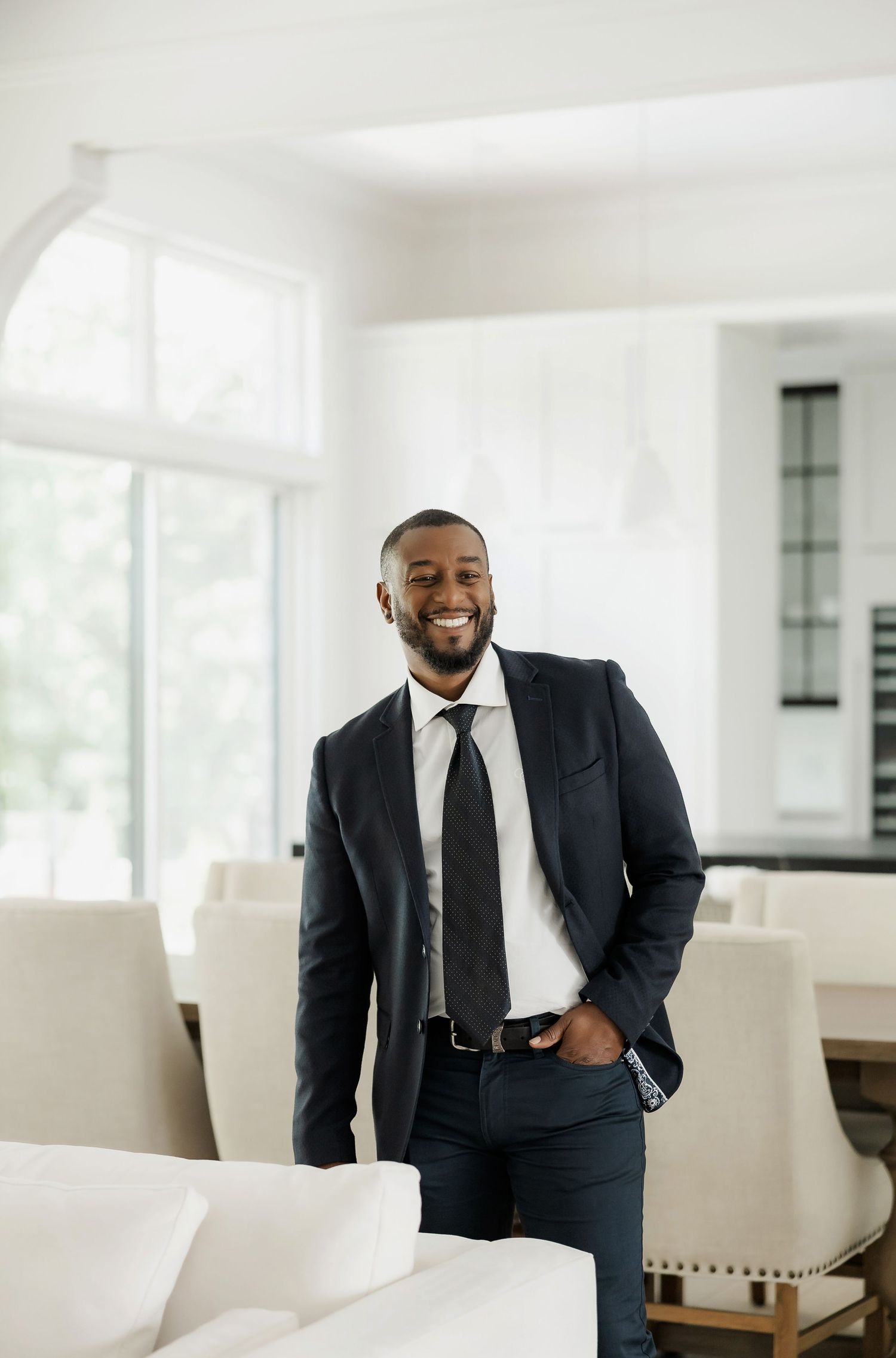 Professional in a dark suit smiling while standing in a bright modern office space.