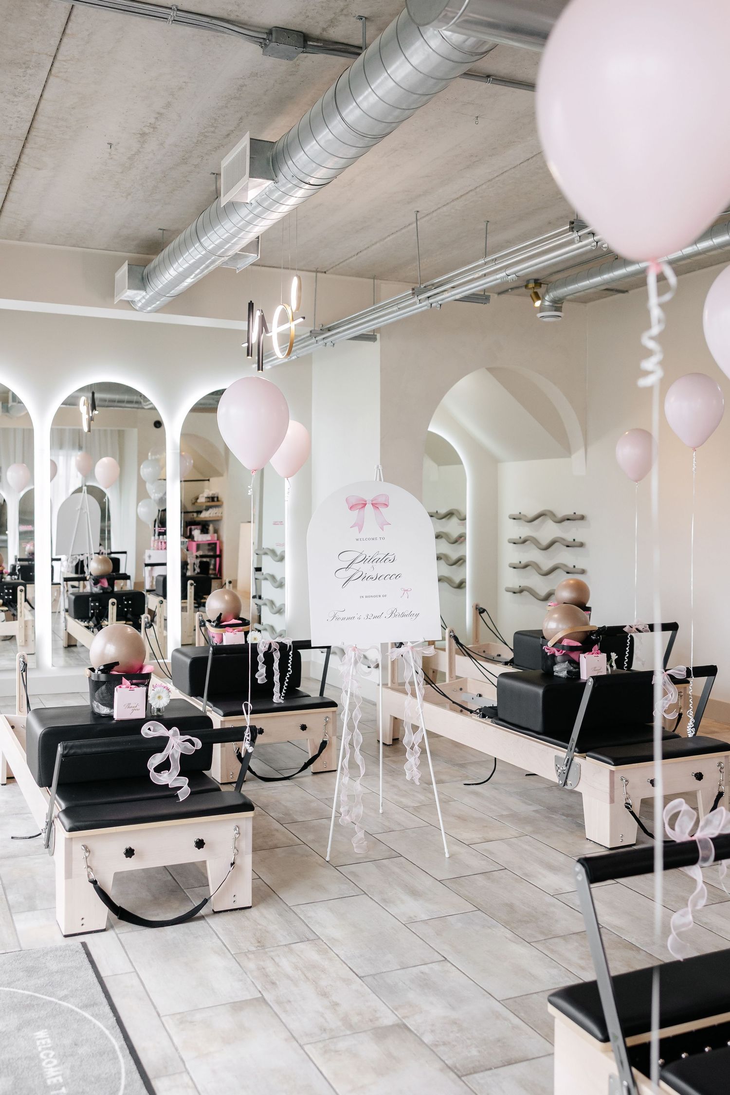 Spacious pilates studio with industrial ceiling and pink balloon decorations.