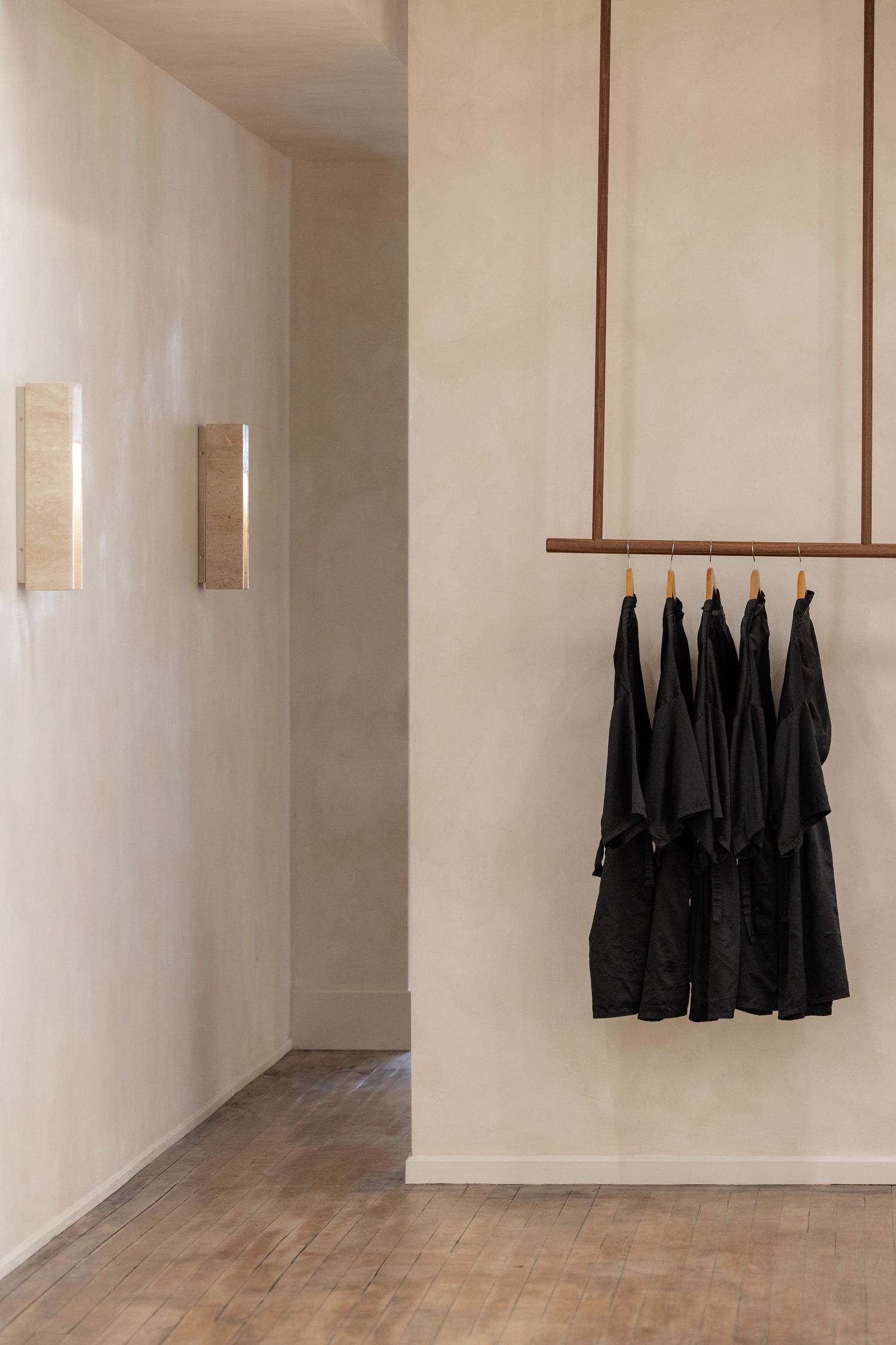 Minimalist white hallway with black aprons hanging on wall hooks.