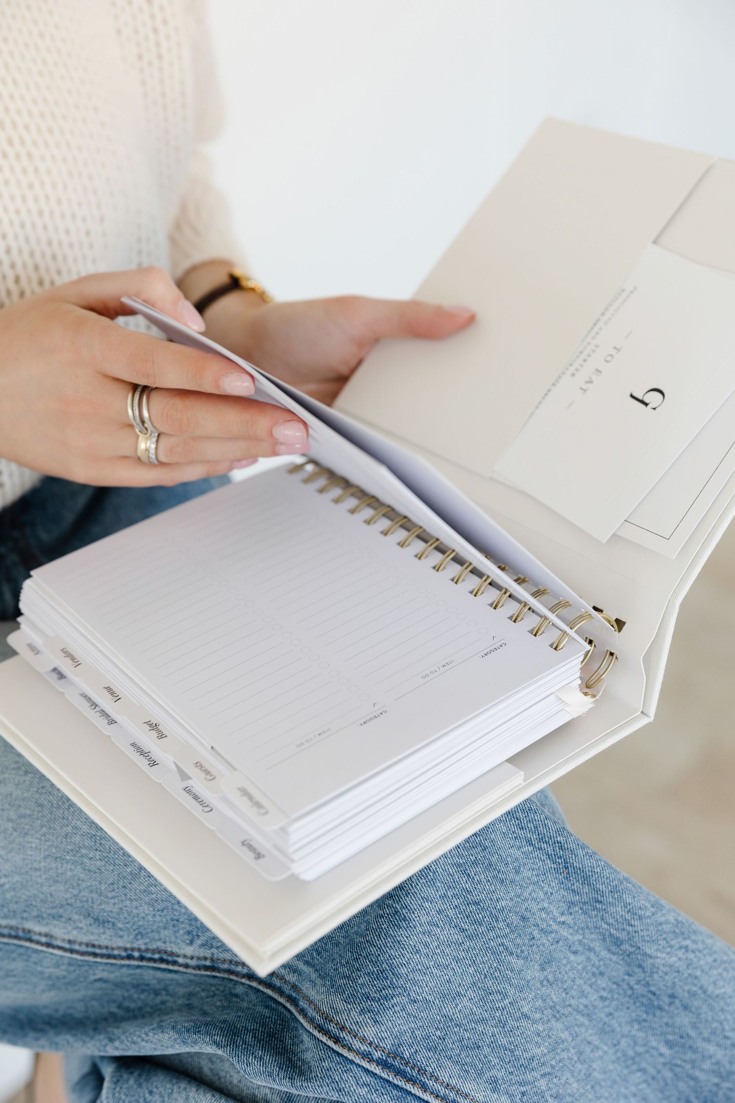 Hands holding pen over spiral notebook with white cover and lined pages.