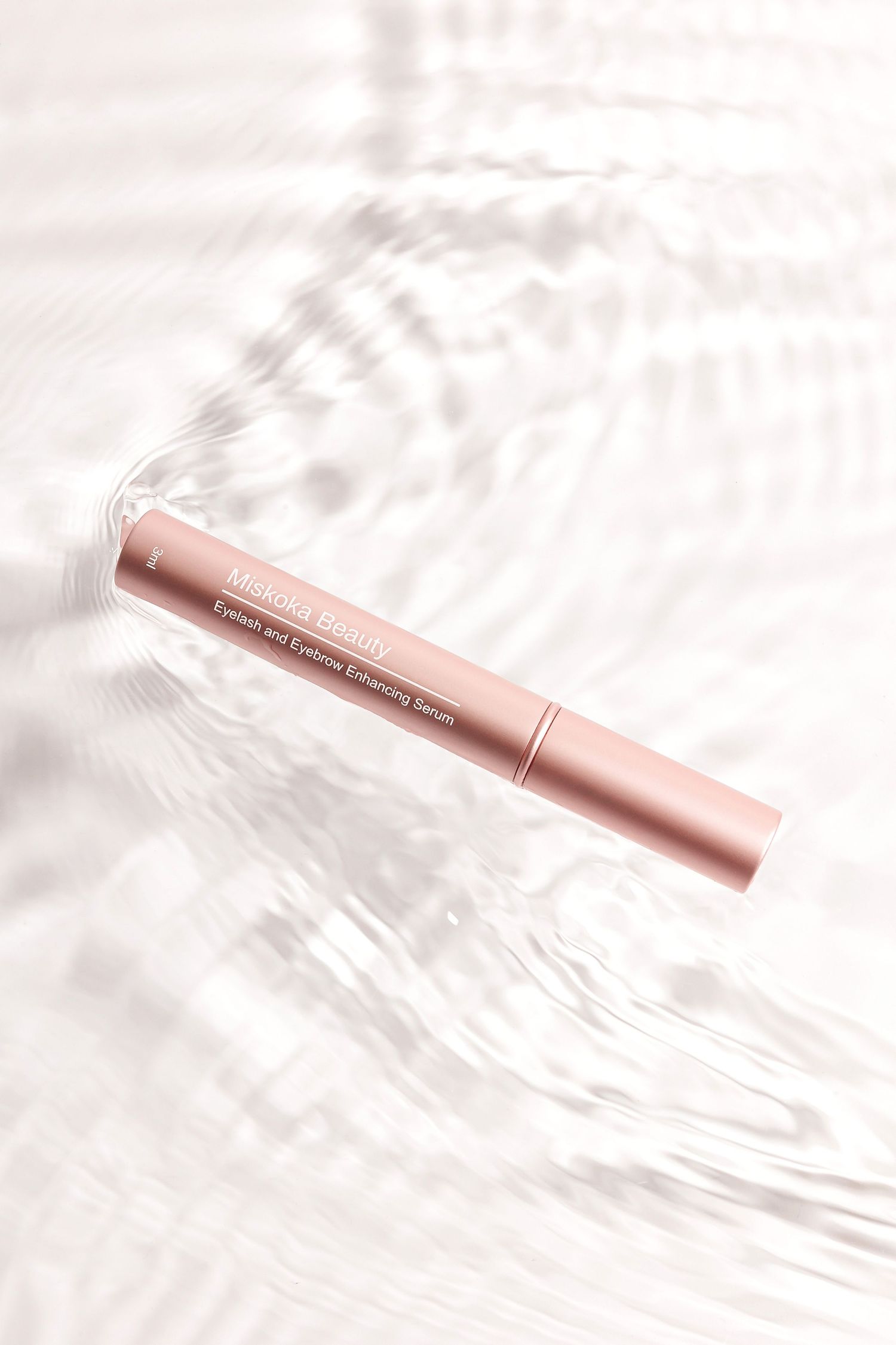 Rose gold makeup pen lying on white textured background with soft shadows.
