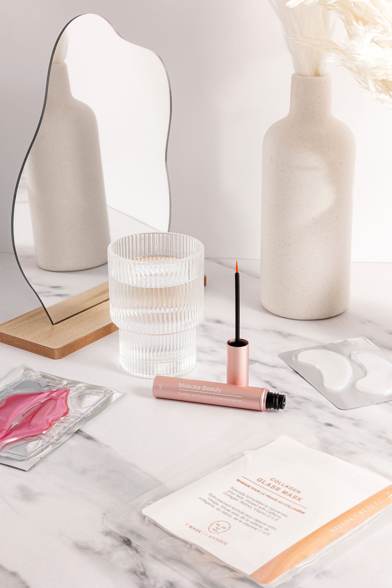 Beauty products and glass accessories styled on marble surface with white ceramic vases.