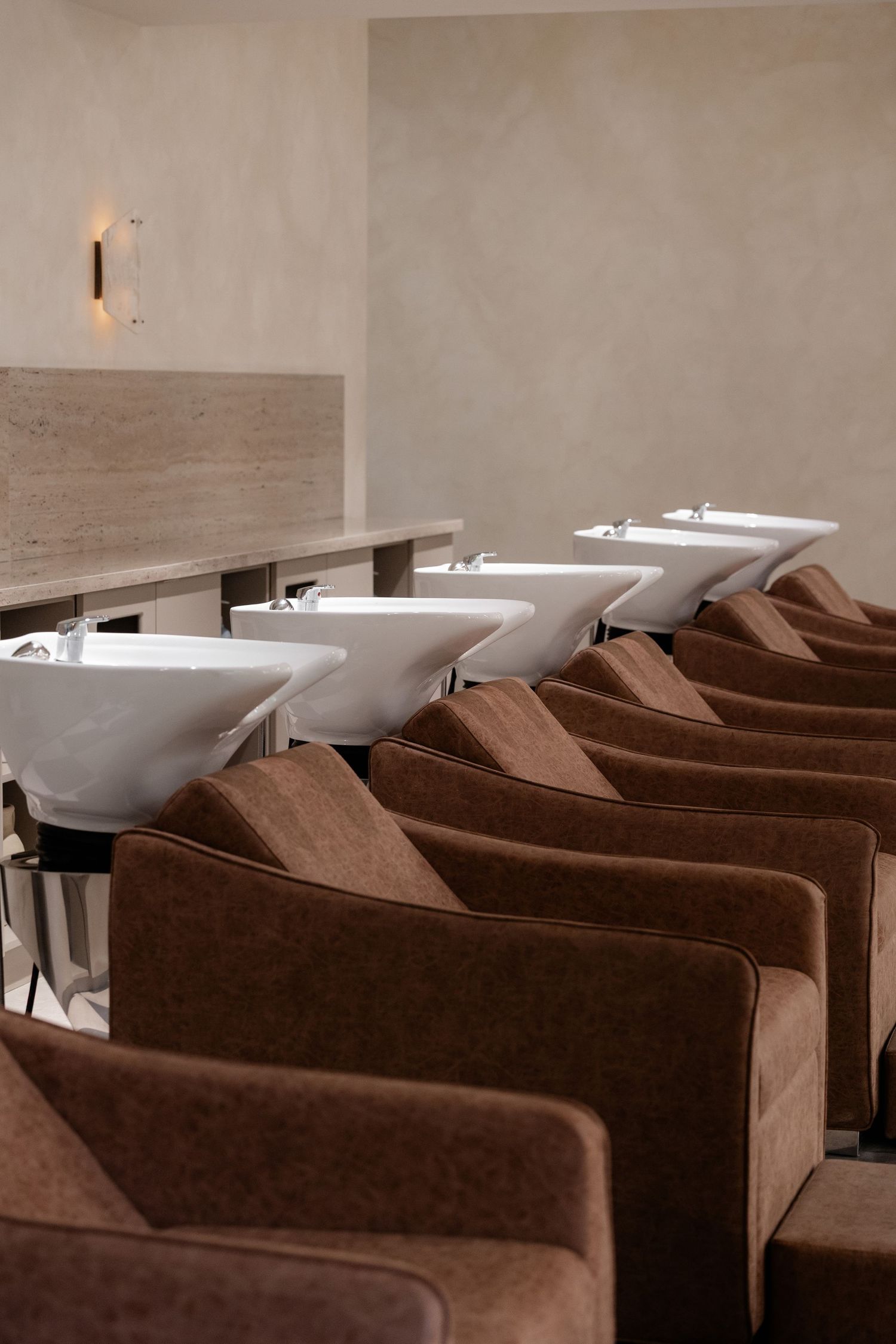 Row of brown velvet chairs at hair washing stations in upscale salon.