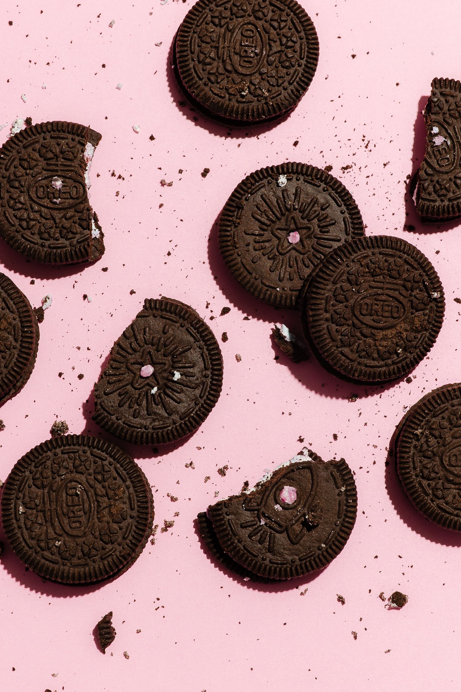 Chocolate sandwich cookies scattered on pink background with crumbs.