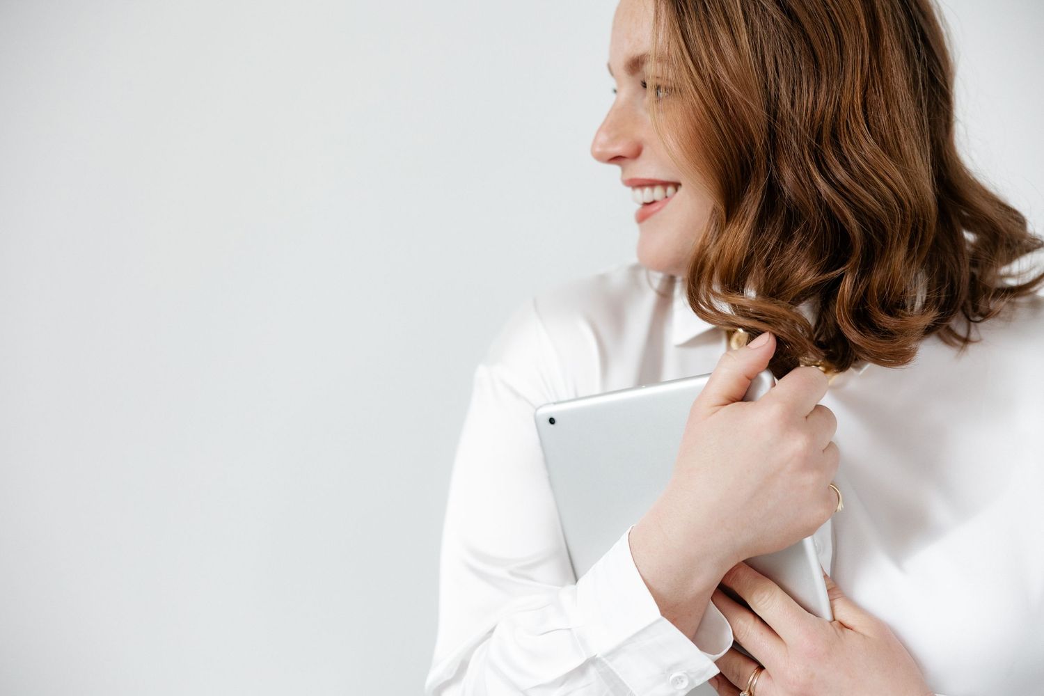Person in white holding a tablet device against a minimalist white background.
