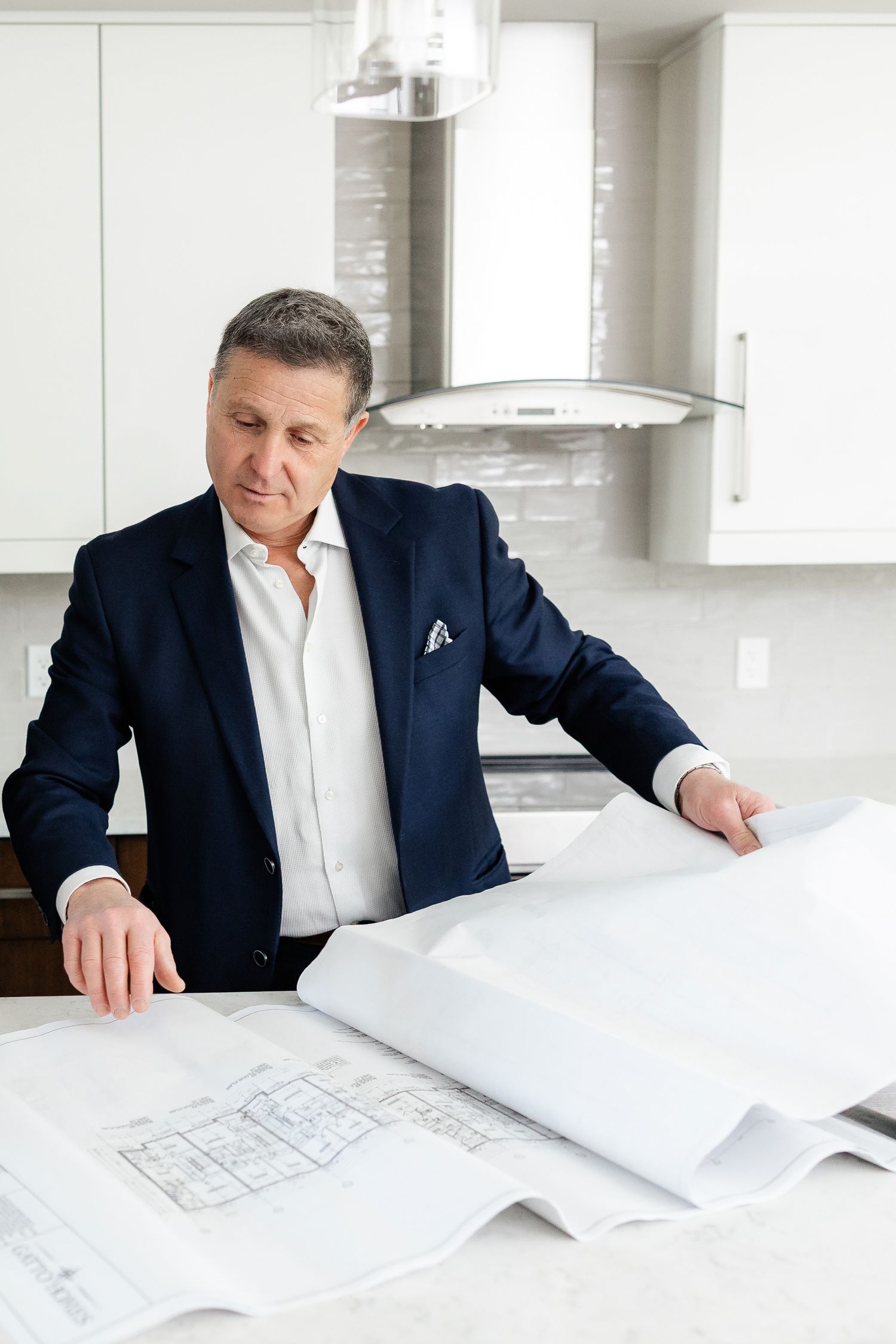 Professional in navy suit examining architectural blueprints on white kitchen counter.