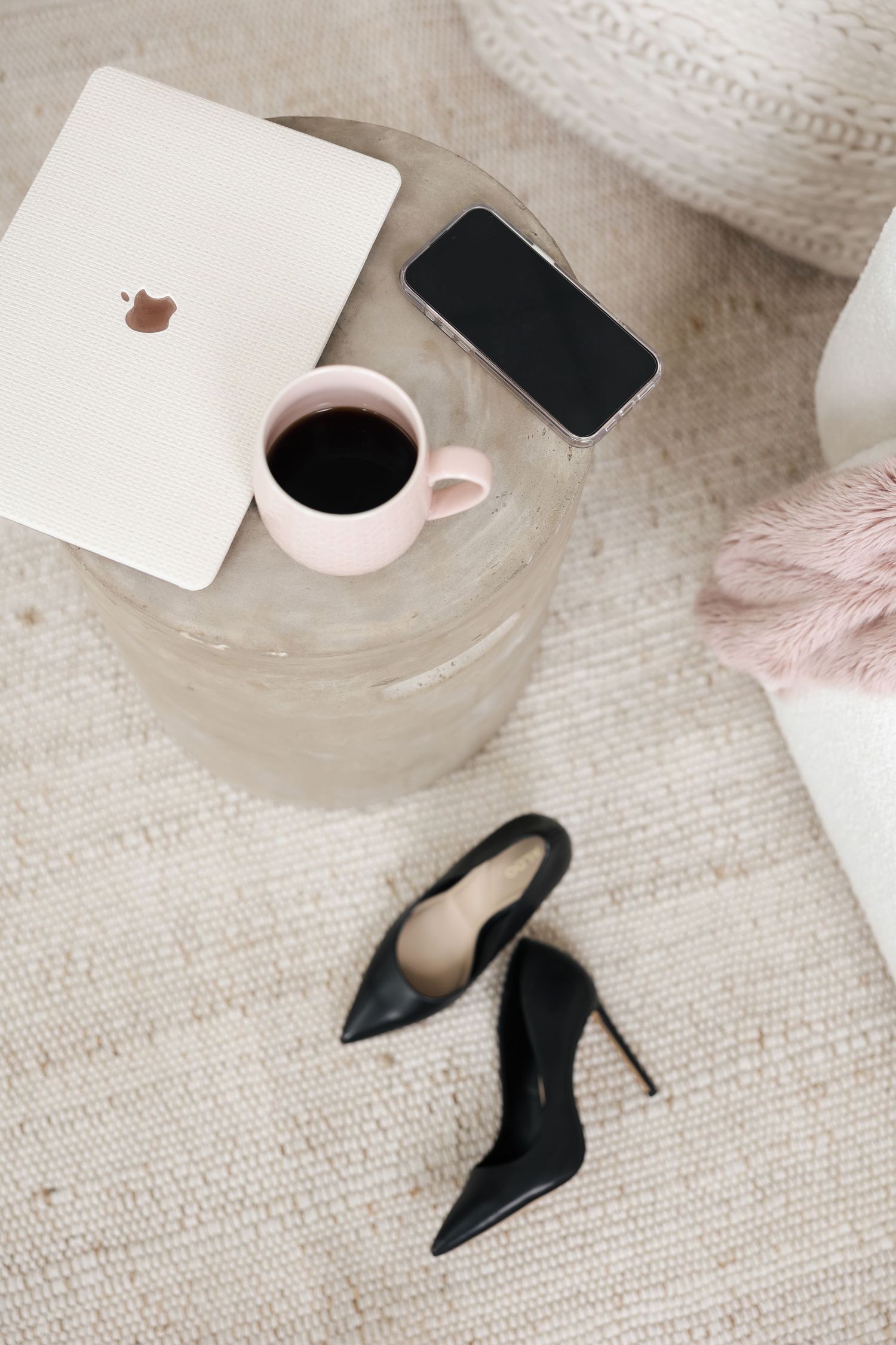 Flat lay of coffee cups, phones, and black high heels on a textured beige carpet.