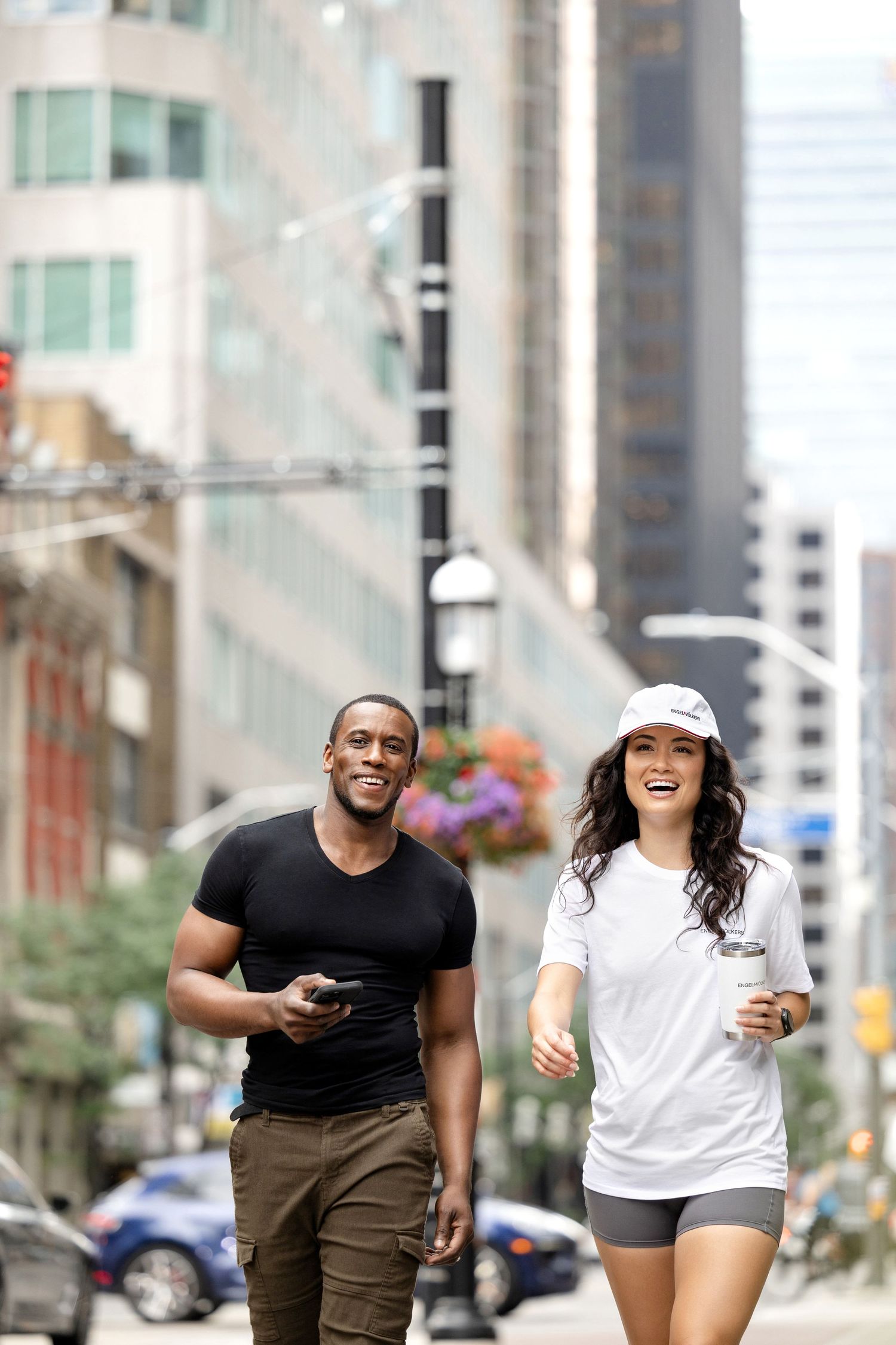 Two people laughing while running together on an urban sidewalk.