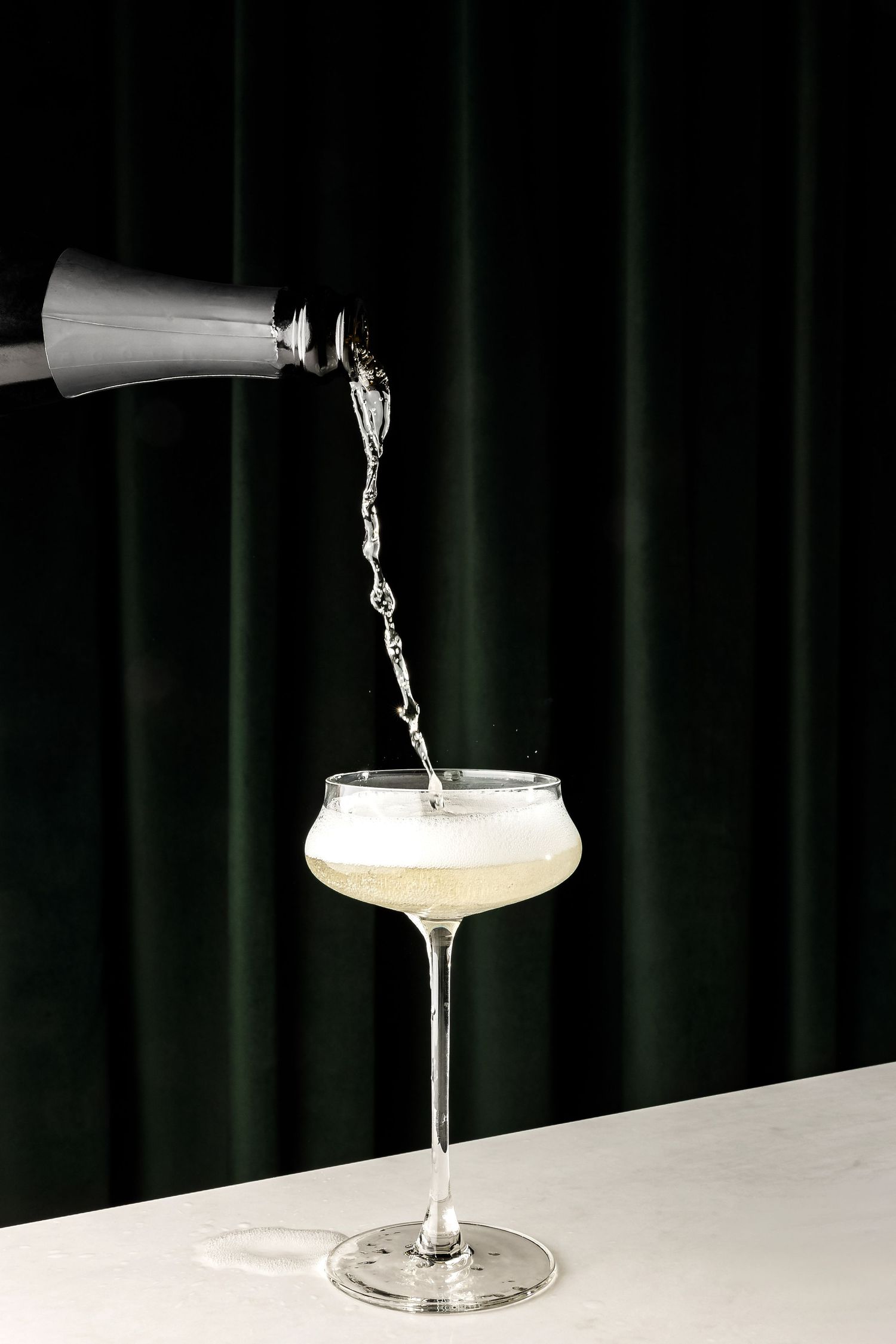 A cocktail being poured from a silver shaker into an elegant coupe glass.
