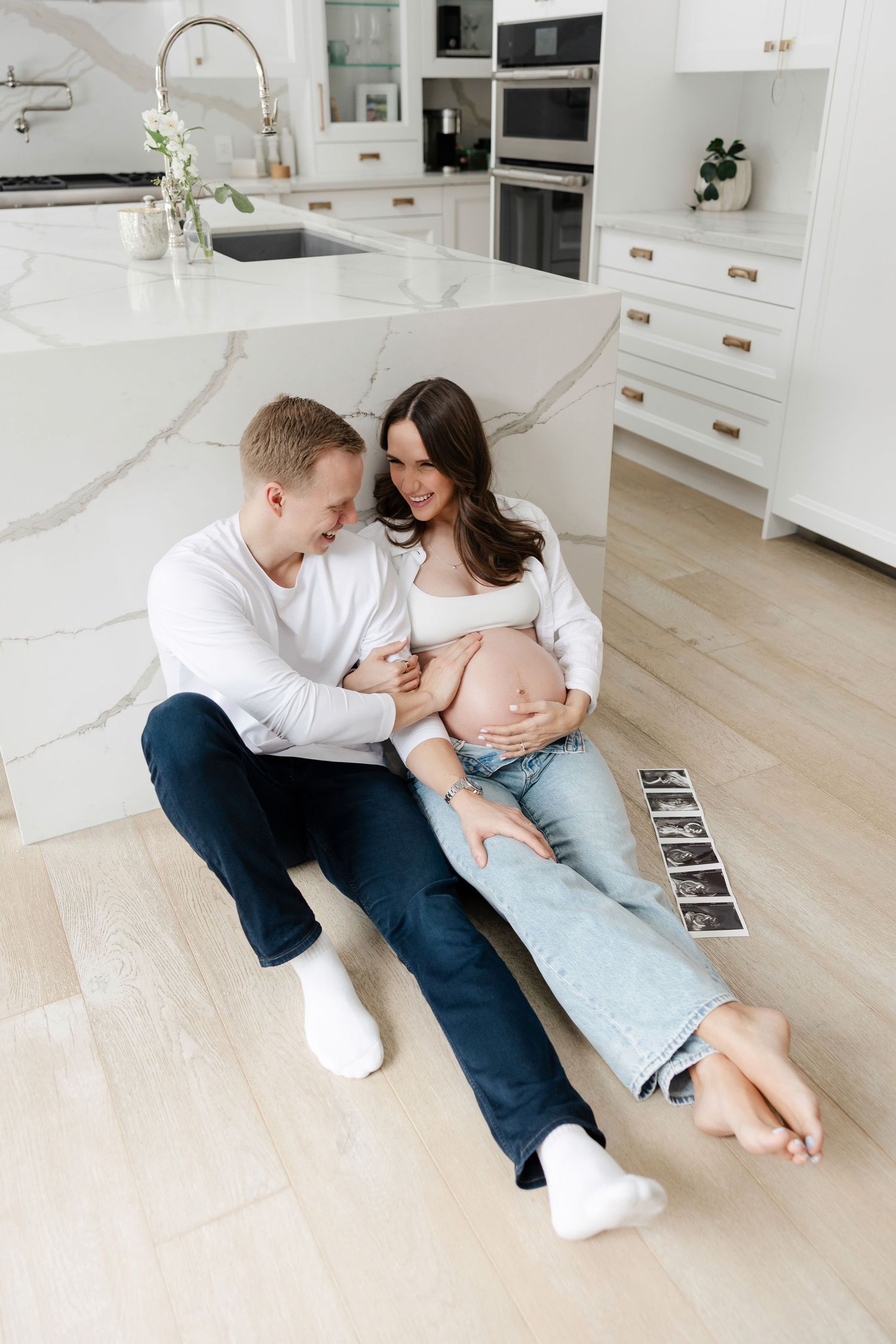 A tender maternity moment shared on a kitchen floor with white cabinets and marble countertops.