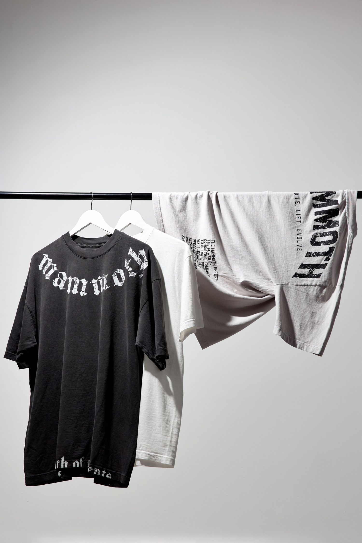 Black and white t-shirts hanging on clothing rack against light background.