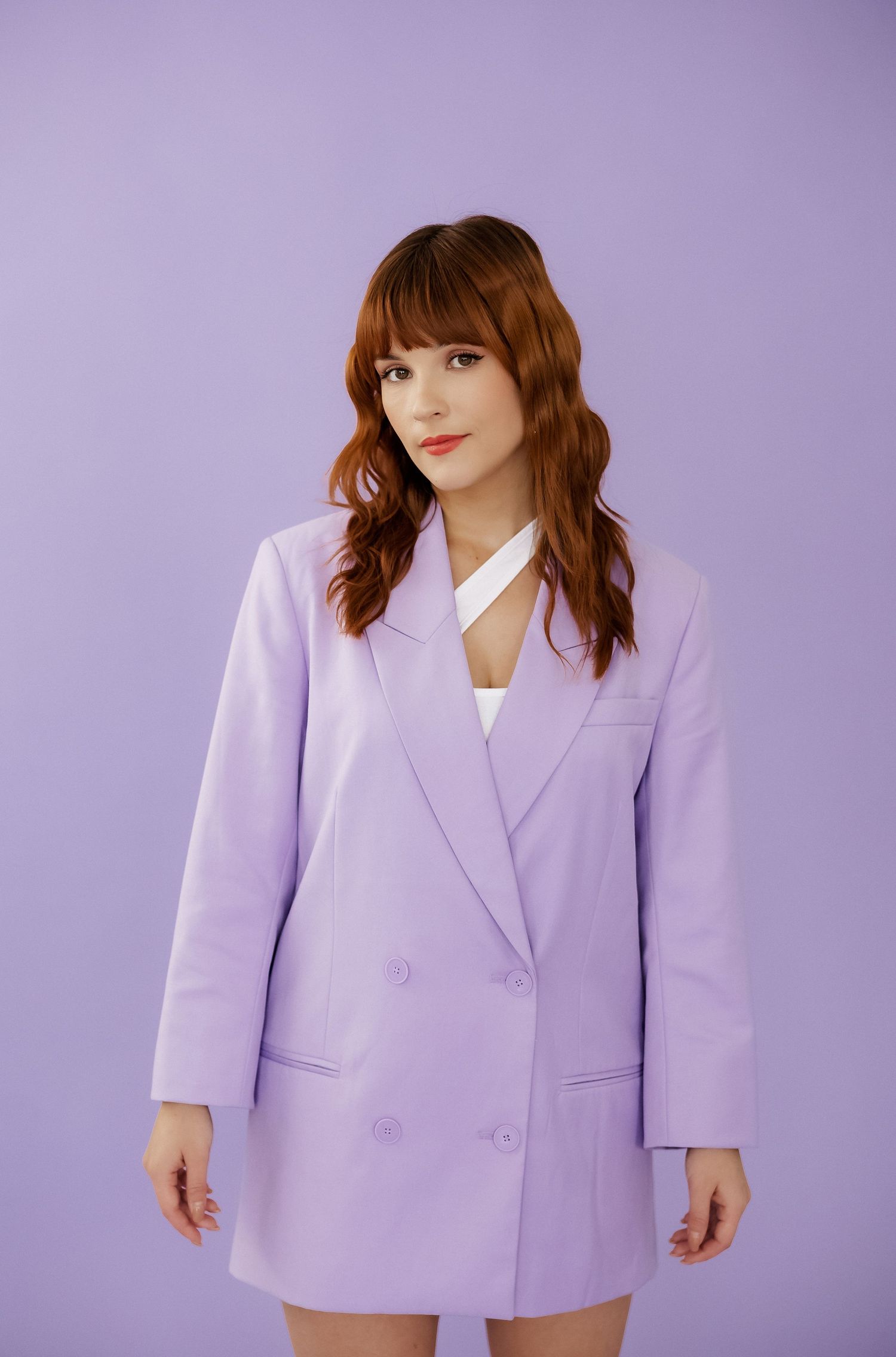 Model wearing oversized lilac blazer poses against purple background in studio setting.
