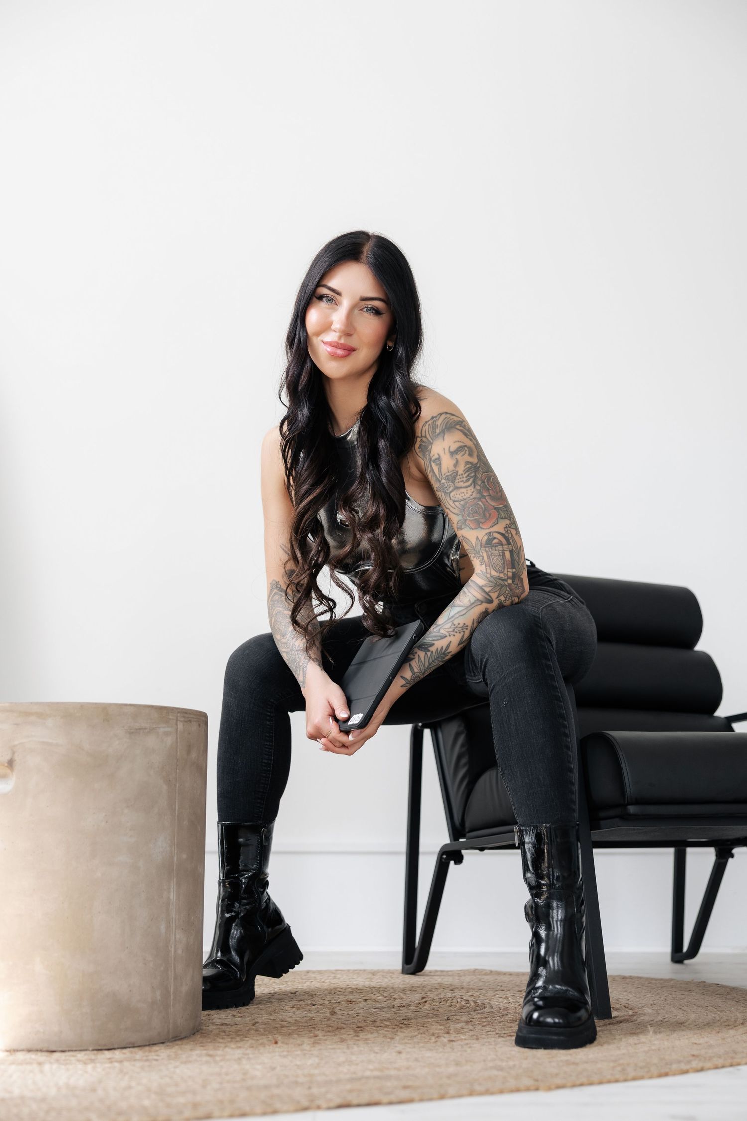 Stylish model seated on black leather chair in modern minimalist setting.