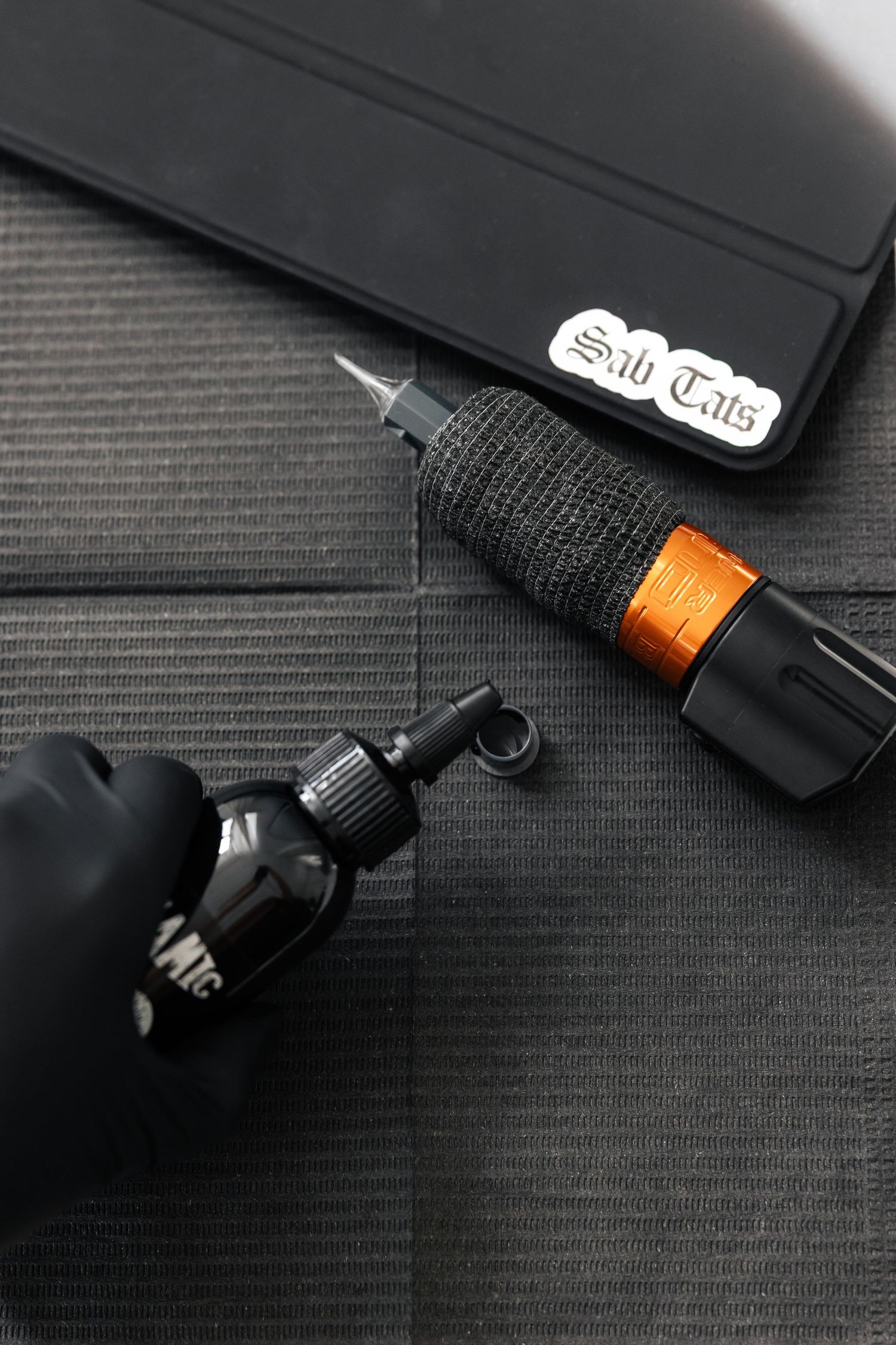 Tattoo equipment including black gloves and machine on dark surface.