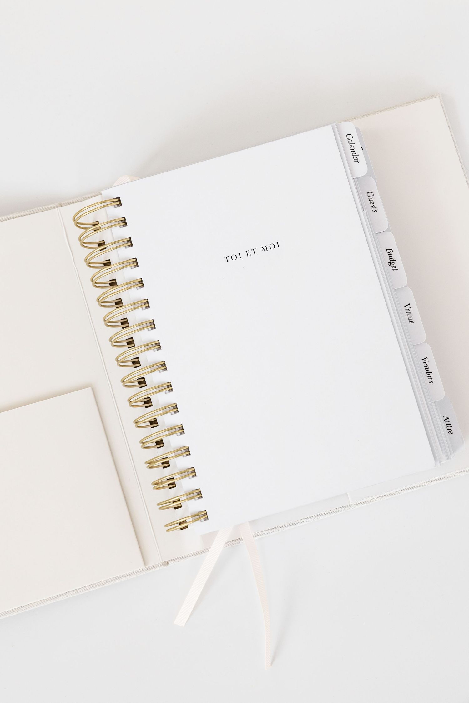 White spiral-bound planner with gold wire binding shown from multiple angles on white background.