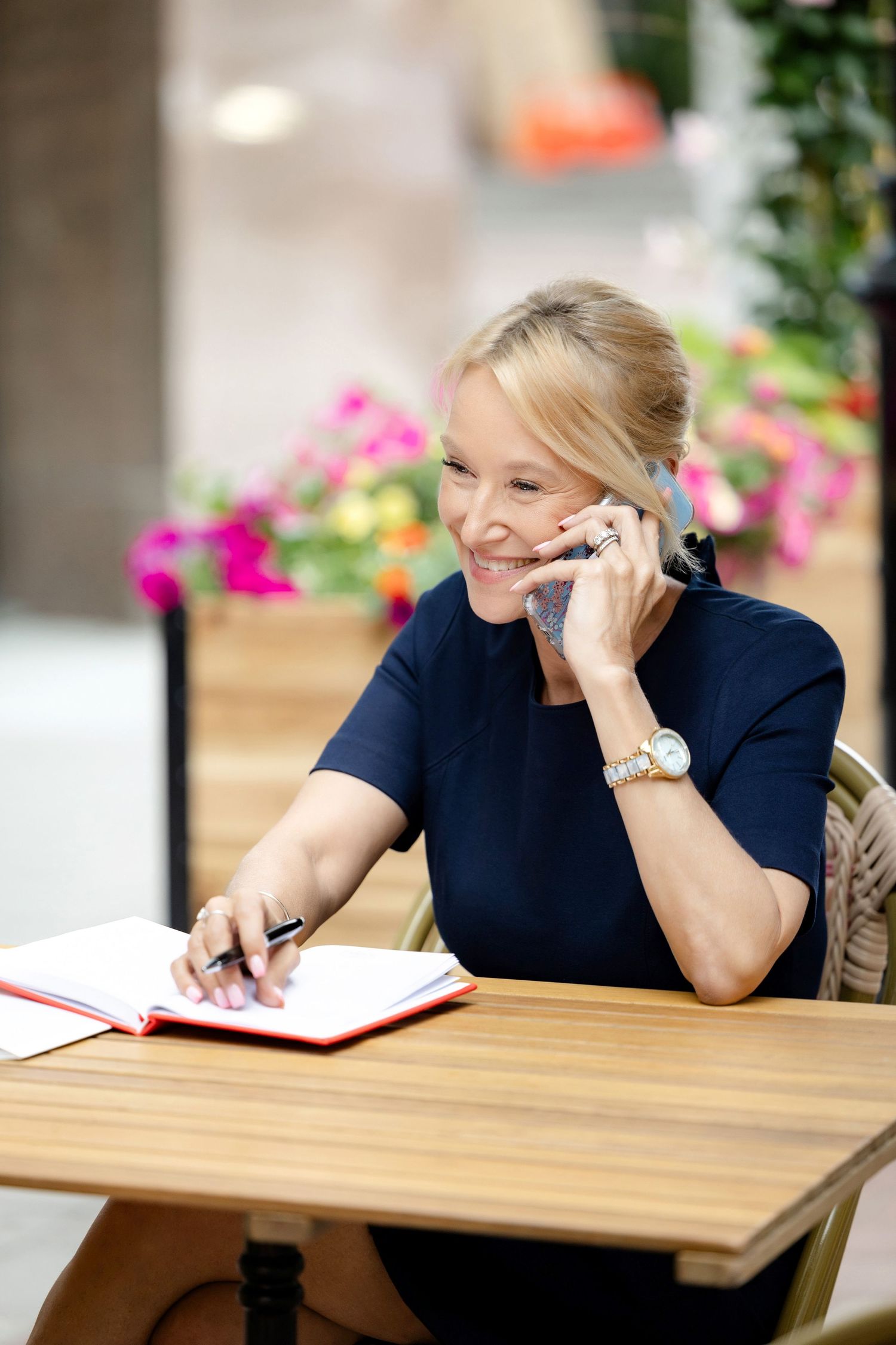 Person in navy blue sitting at wooden table with notebook and phone.