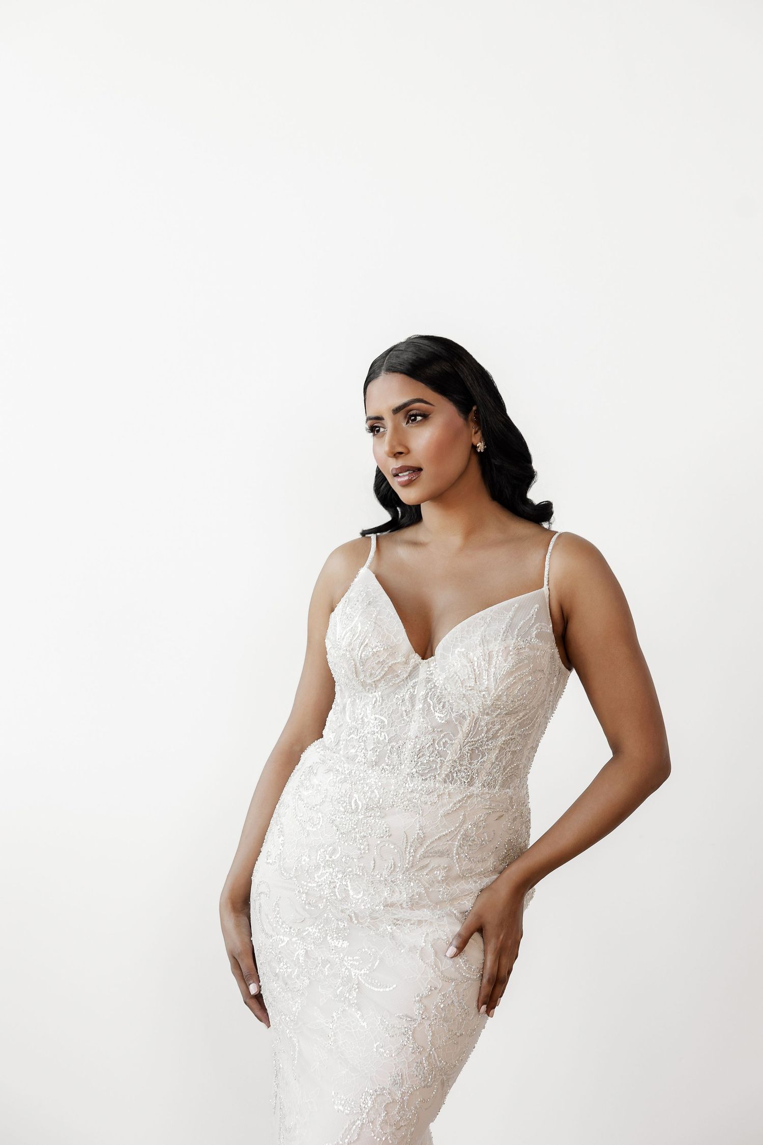 Model poses in fitted lace wedding dress with sweetheart neckline against white background.