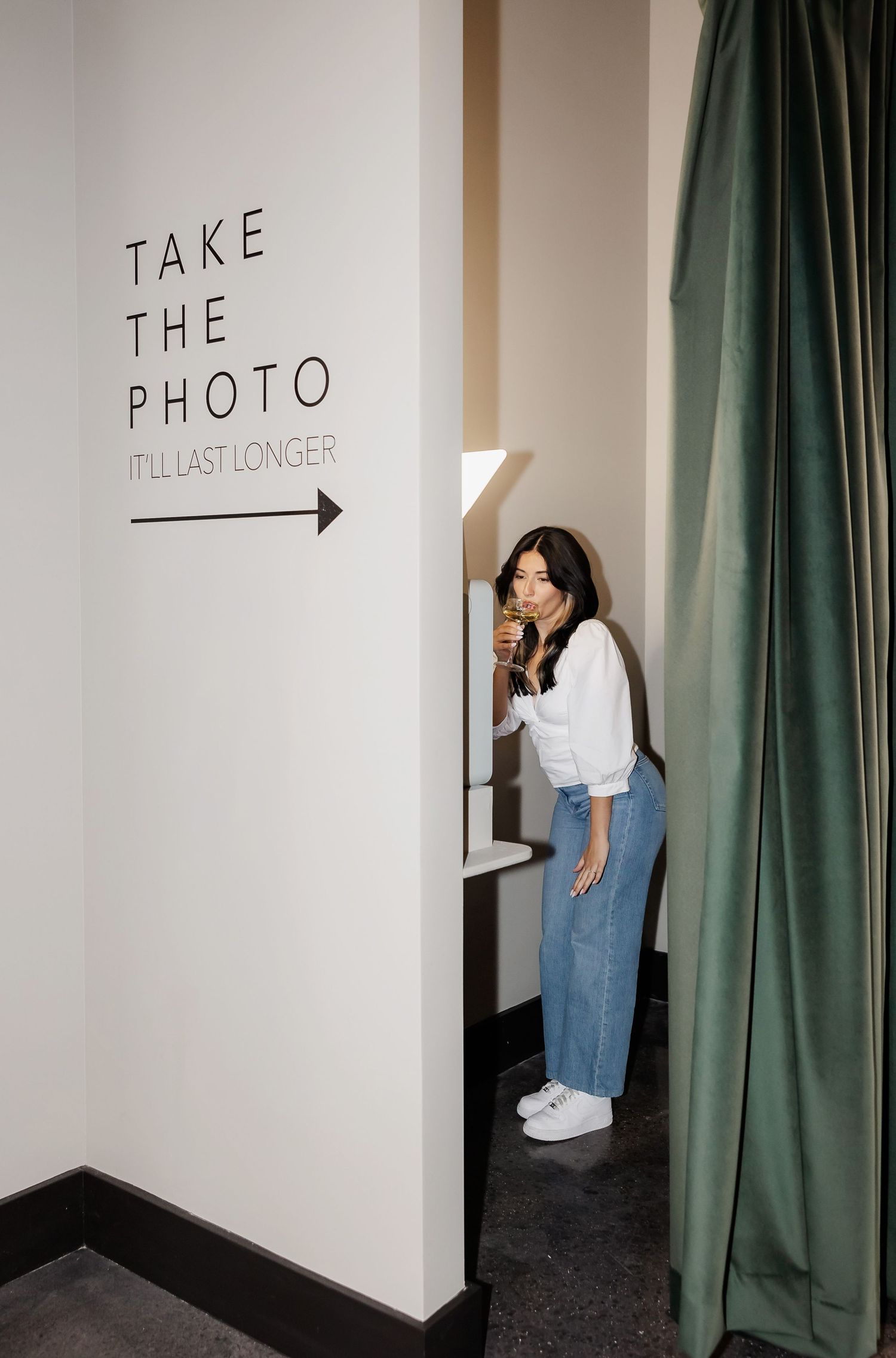 People taking photos near a wall with directional signage and green curtains.