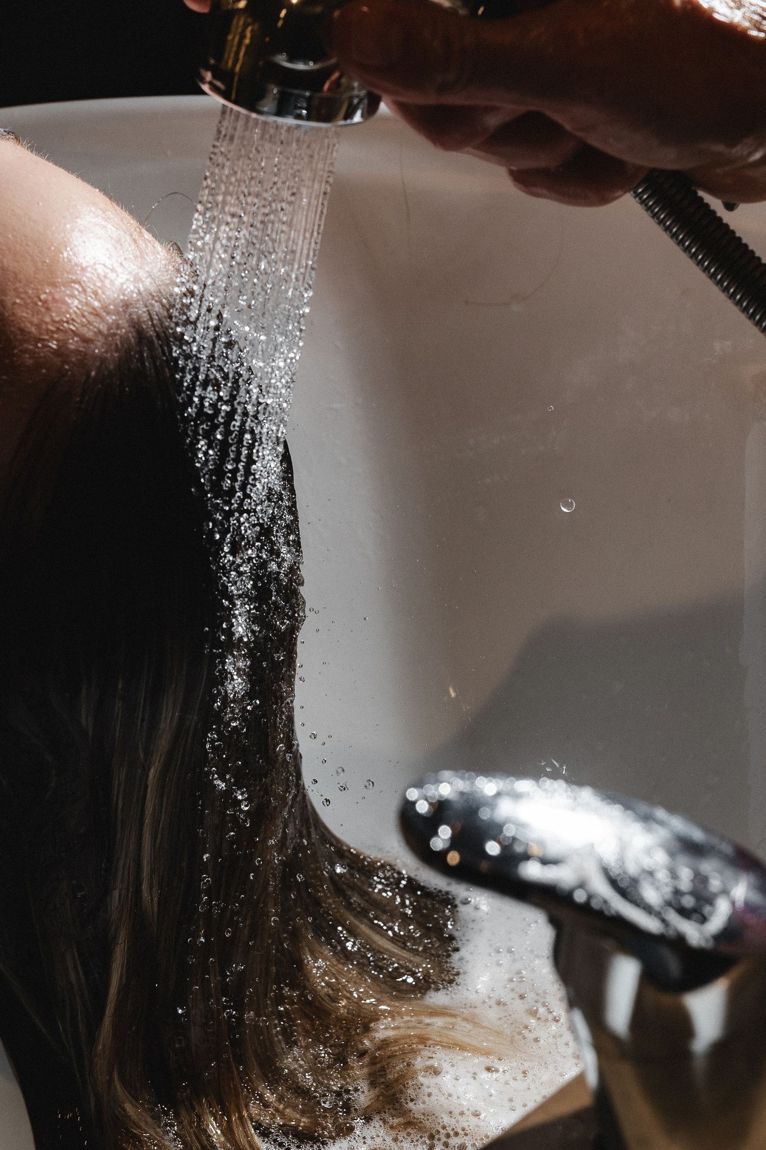 Water spraying over dark wet hair in a salon sink.