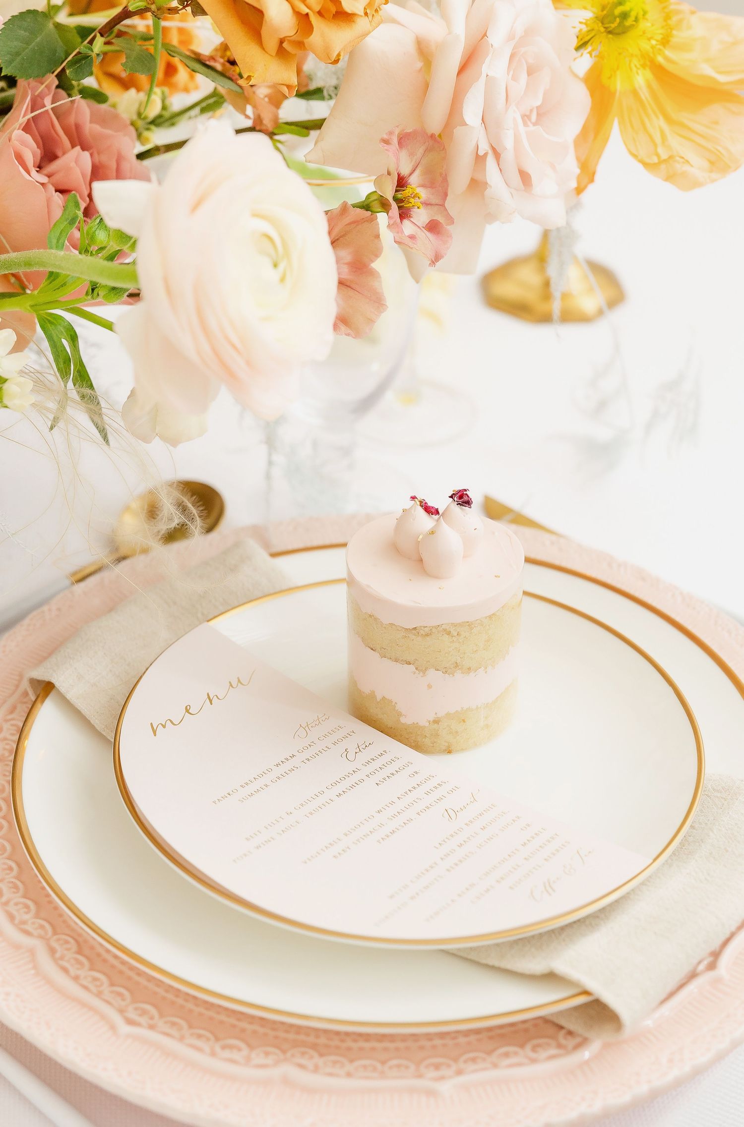 Wedding table setting with peach florals and gold-rimmed plates featuring menu cards.