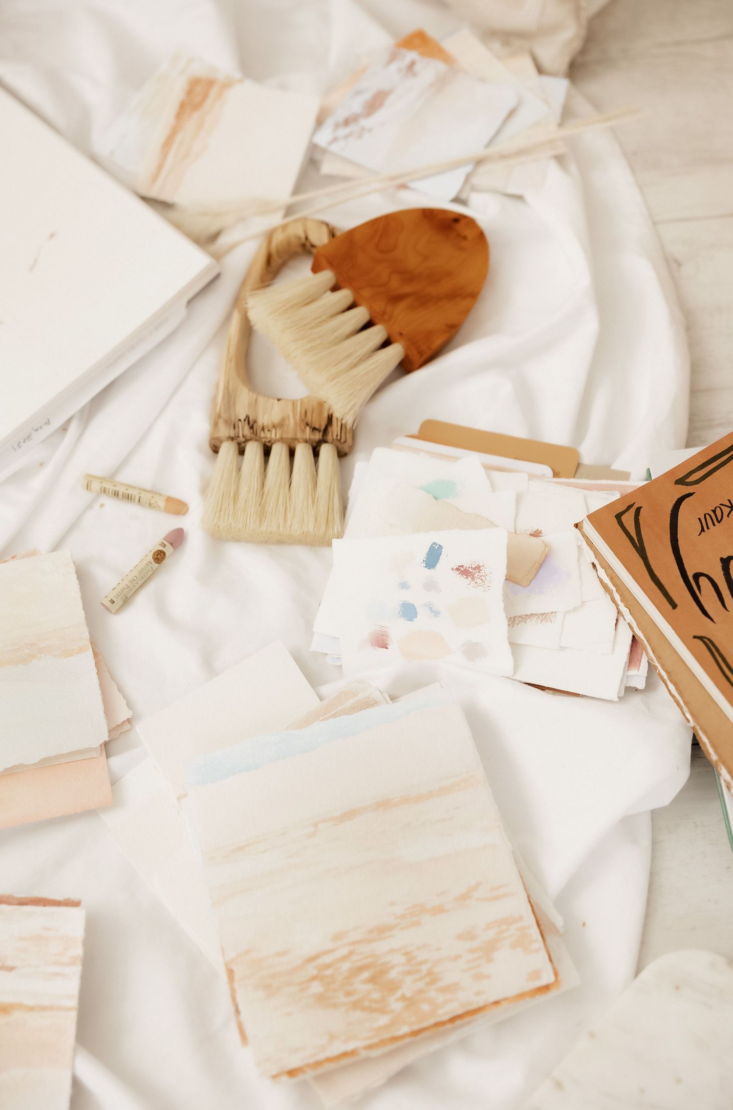 Artistic flatlay of paintbrushes and creative materials on white fabric background.