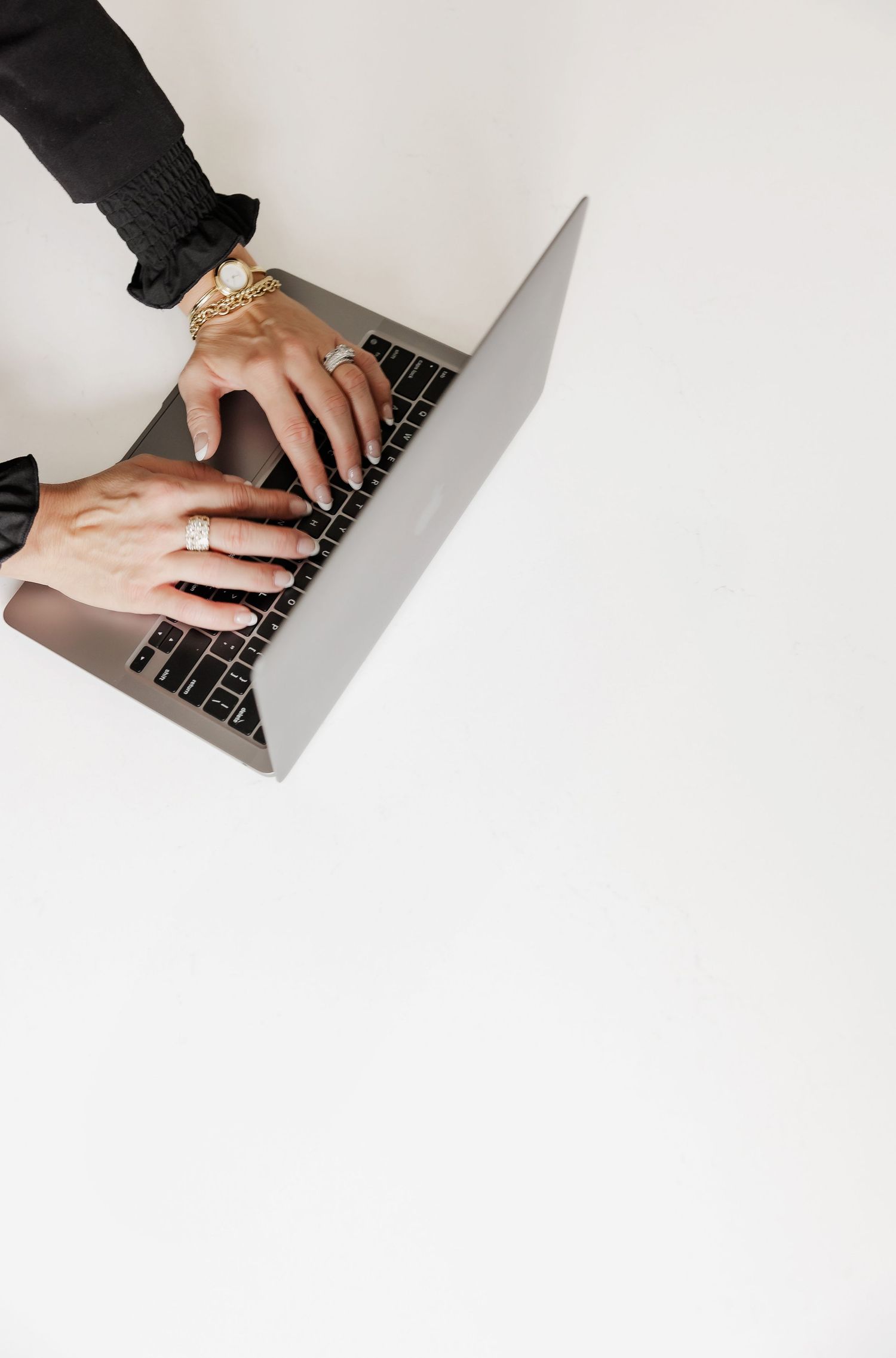 Close-up view of hands typing on a MacBook keyboard against white background.