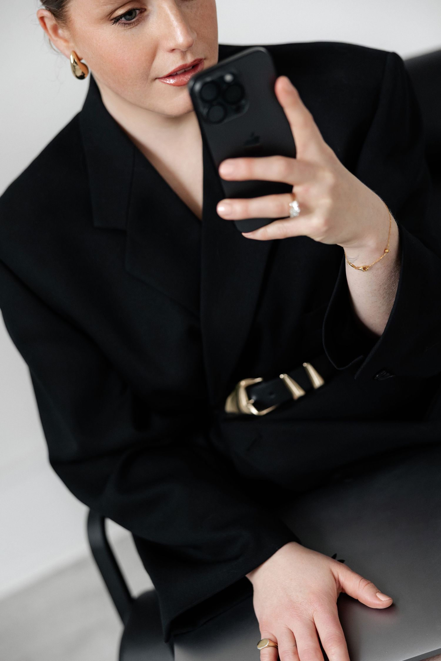 Close-up shot of hands holding iPhone while wearing black blazer with gold belt.