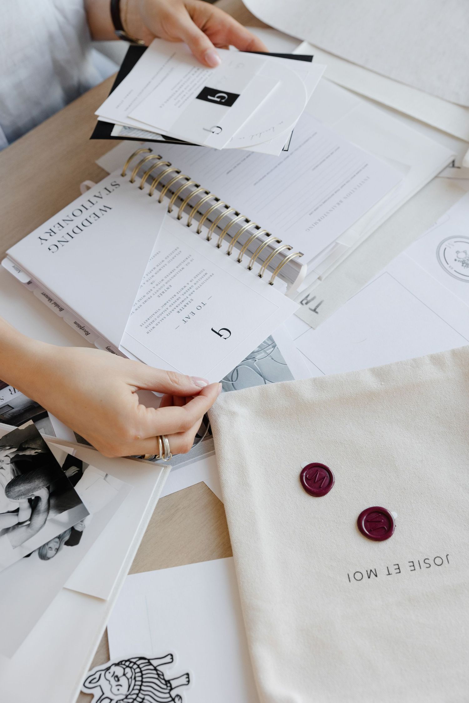Hands arranging white paper documents with red wax seals on a wooden desk.