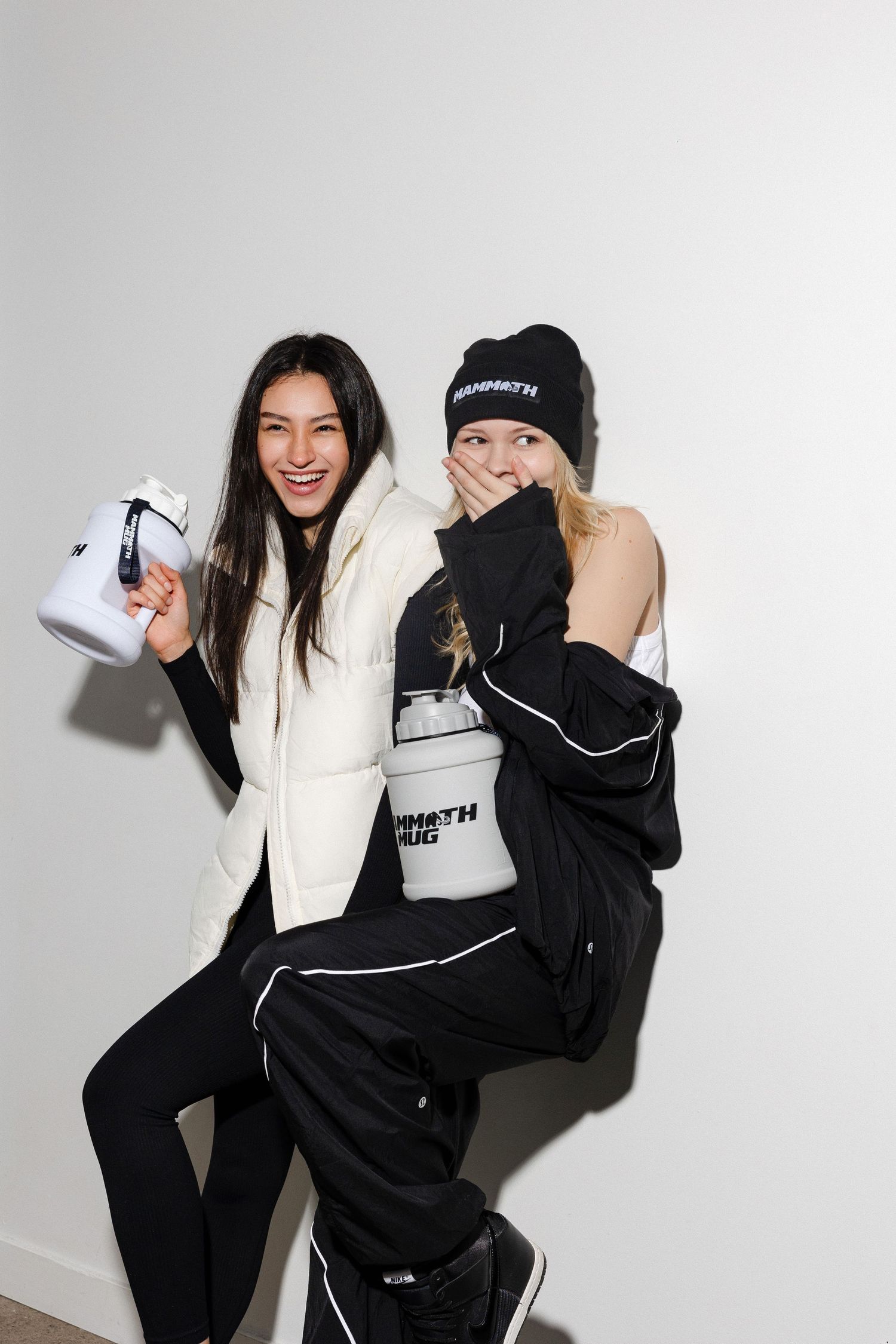 Models in contrasting black and white outfits playfully pose with branded white containers.