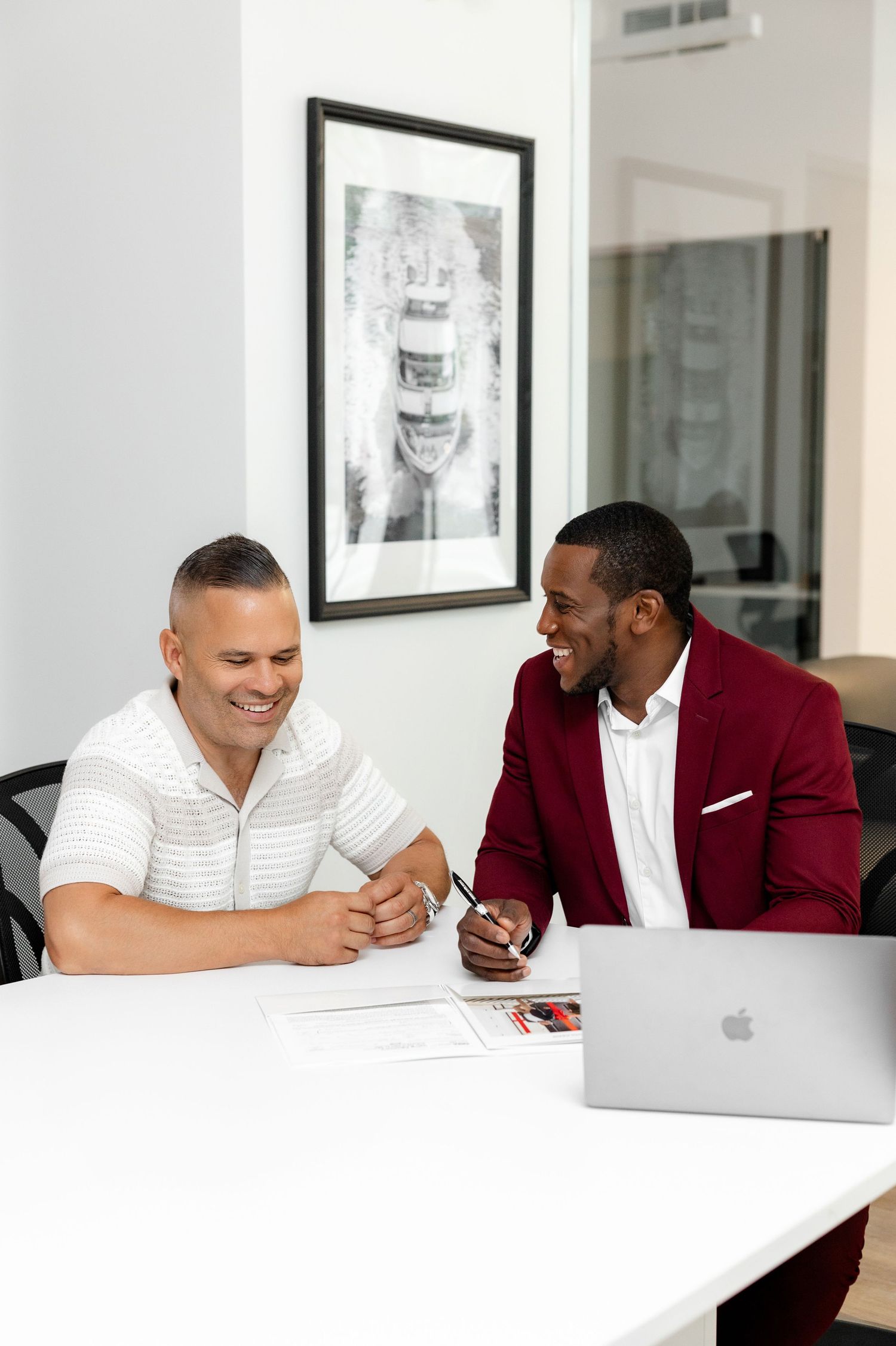 Two people signing documents at a modern white desk with a laptop.