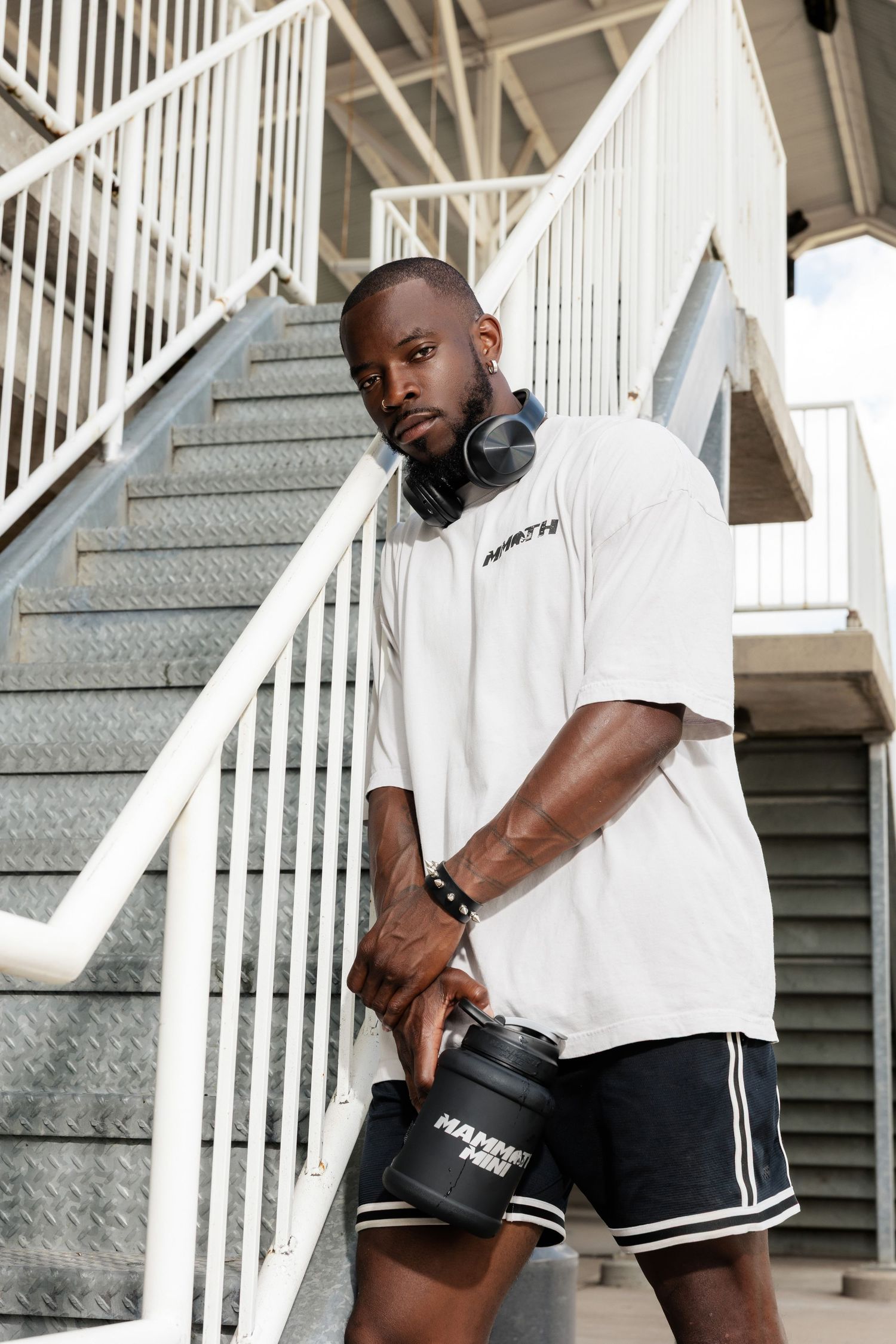 Person in white t-shirt and black shorts with headphones against white staircase.
