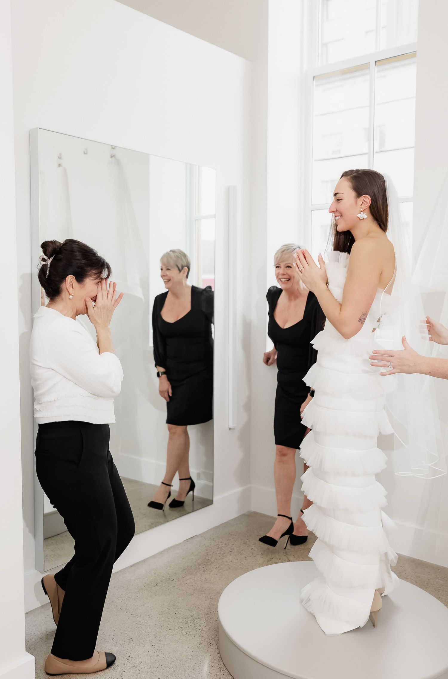 Emotional moment during a wedding dress fitting with stylists and attendees in a bright studio space.