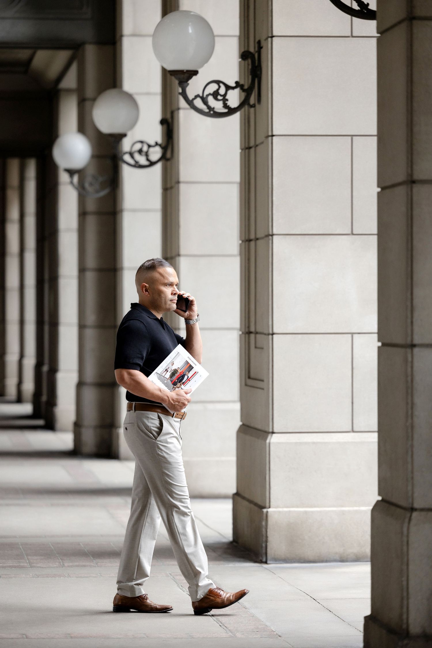 Person walking and talking on phone in a columned architectural corridor.