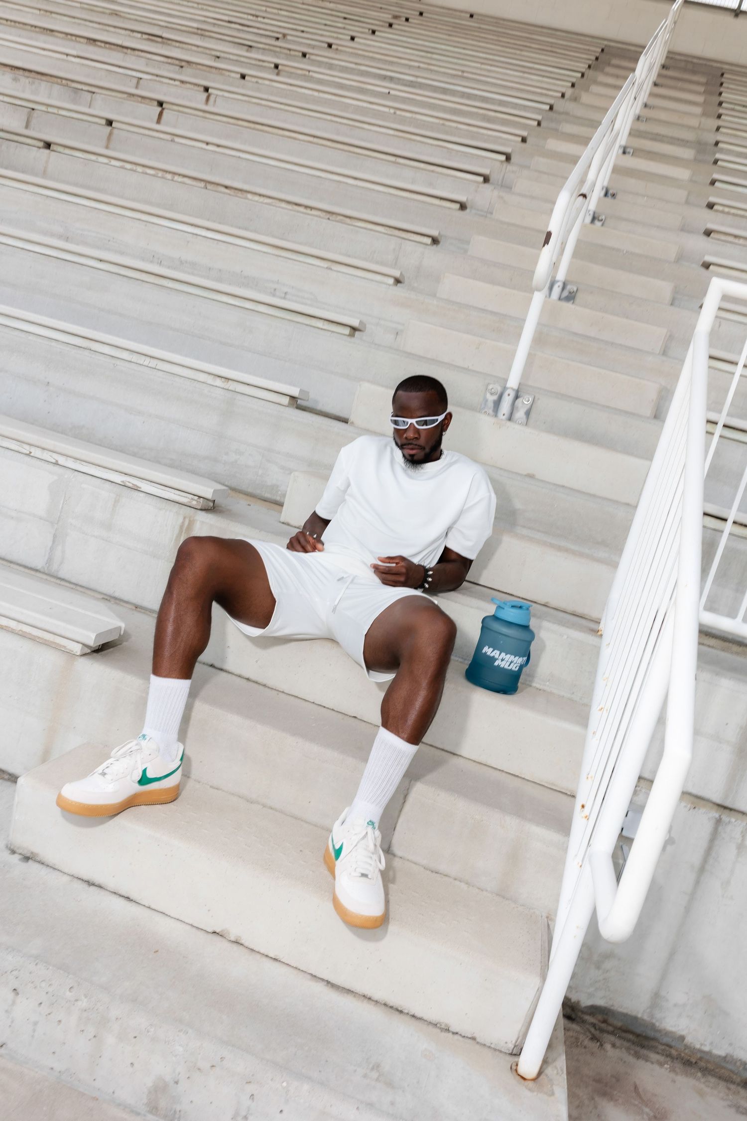 Athletic figure in white outfit lounging on concrete stadium steps with blue water bottle.