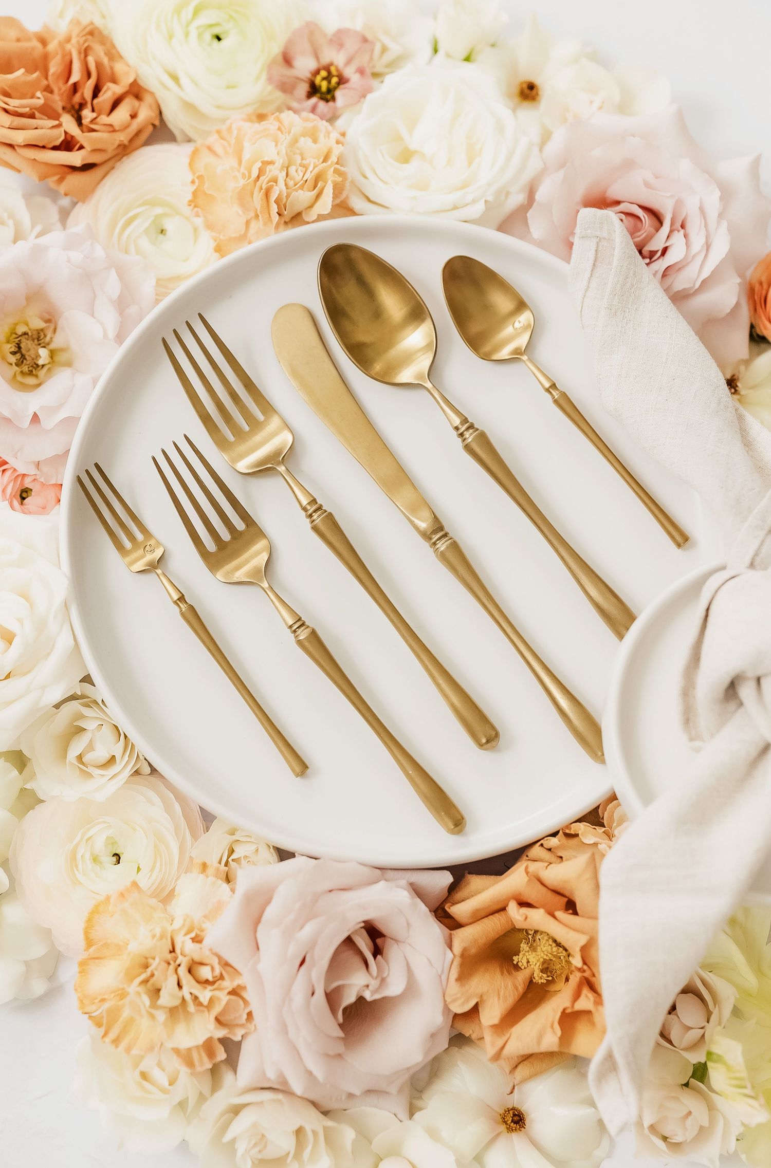 Gold utensils displayed on white plates with romantic floral backdrop.